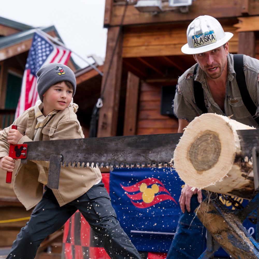 A lumberjack looking on as a young Guest cuts a log using a whipsaw