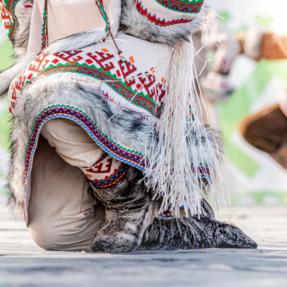 A kneeling Alaskan Native wearing traditional clothing