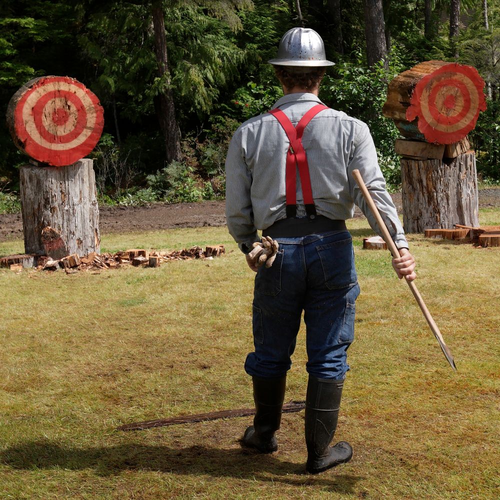 A lumberjack holding an axe while standing in front of 2 axe throwing targets