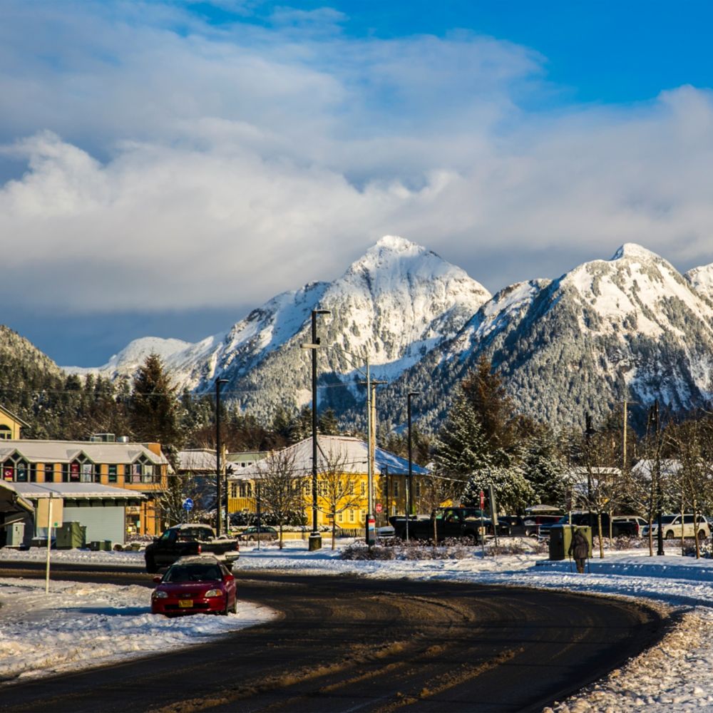 A road traveling through the town of Sitka, Alaska with snowcapped mountains nearby