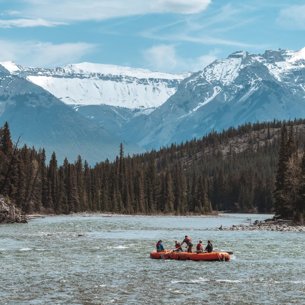 Guest rowing a raft down a river near a forest and snowcapped mountains near Juneau, Alaska