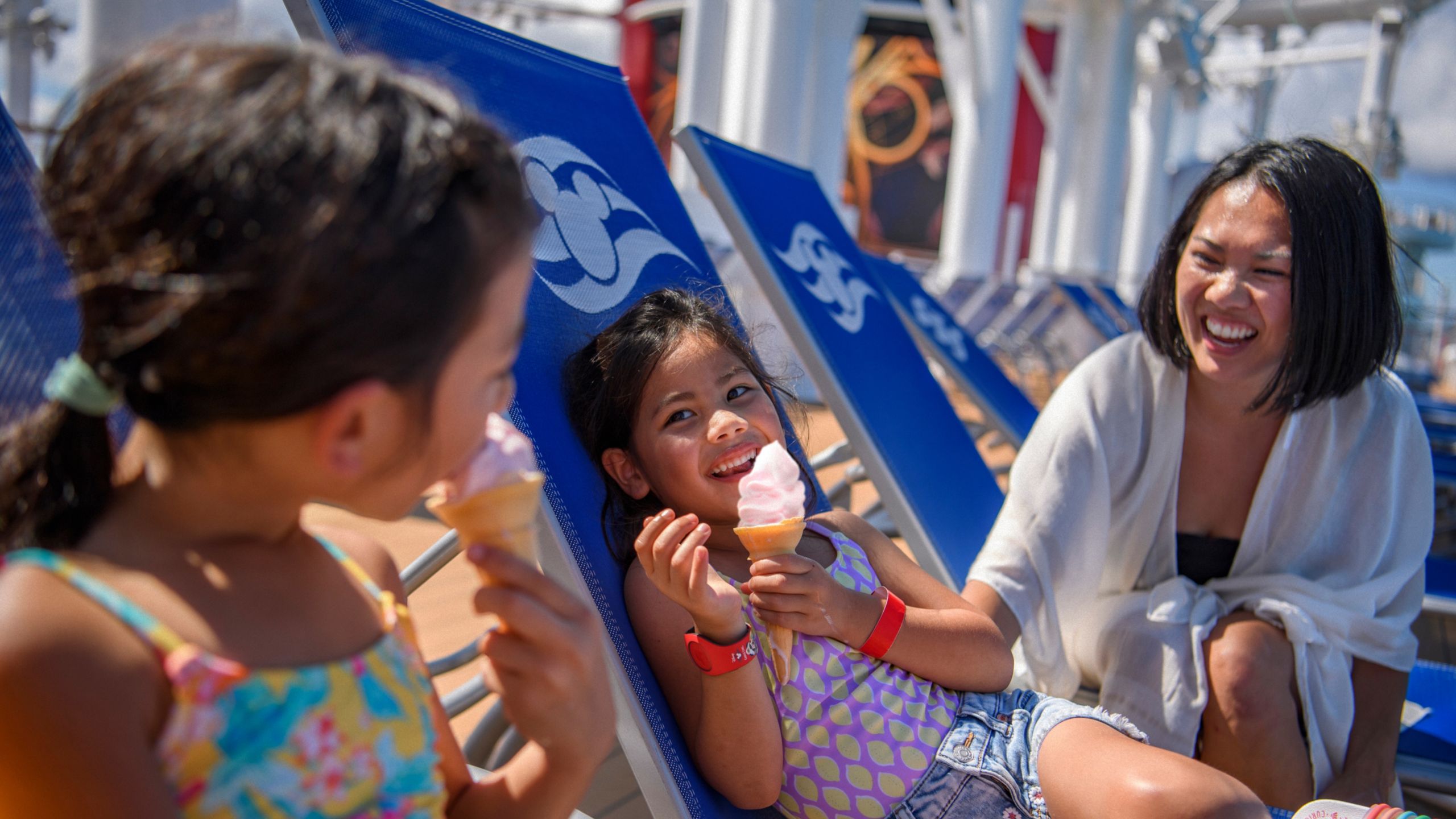 Dos niñas y su madre disfrutando de unos conos de helado y relajándose en reposeras