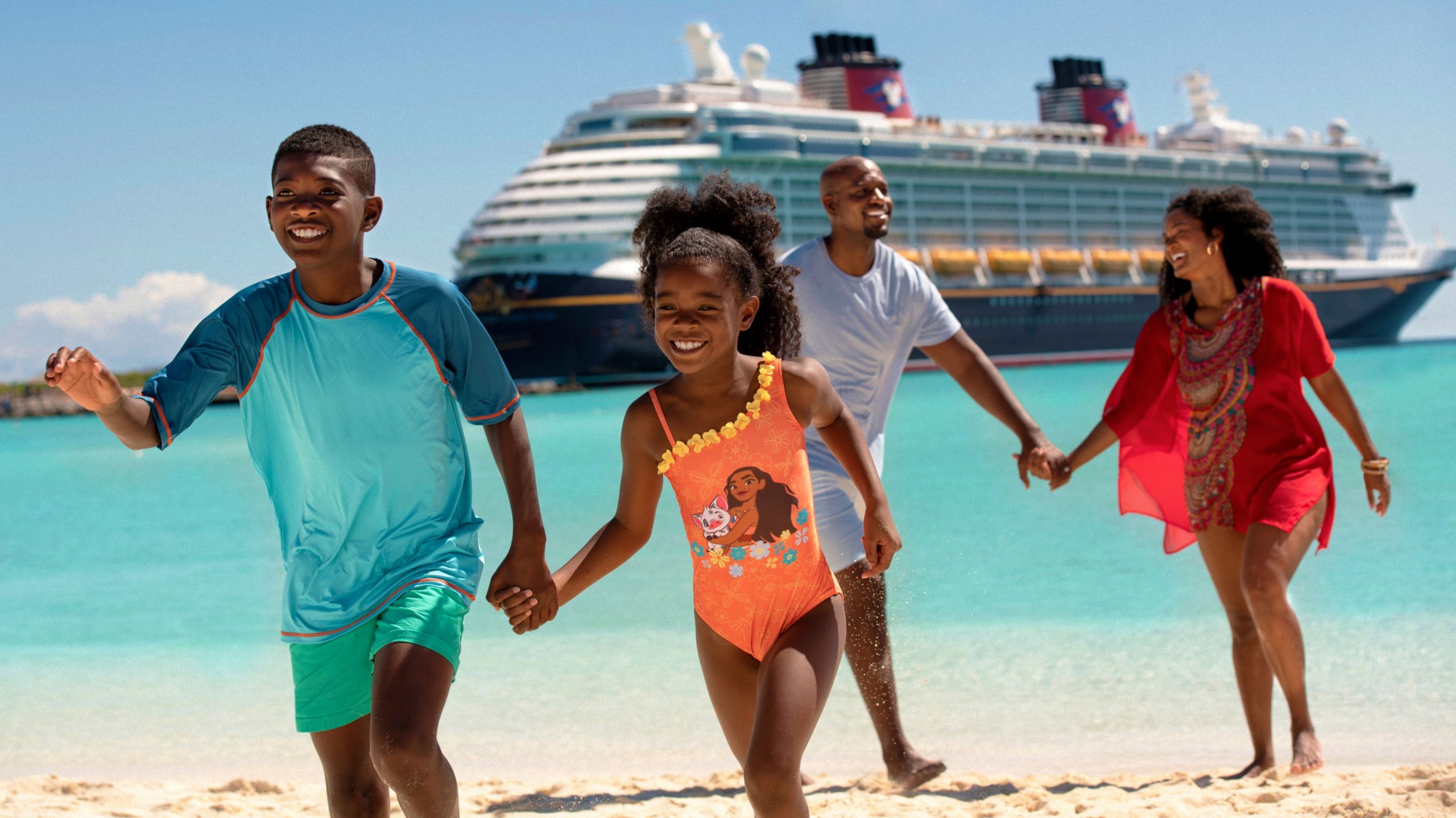 Dos hermanos y sus padres tomados de las manos y corriendo en una playa con un barco de Disney Cruise Line a la distancia