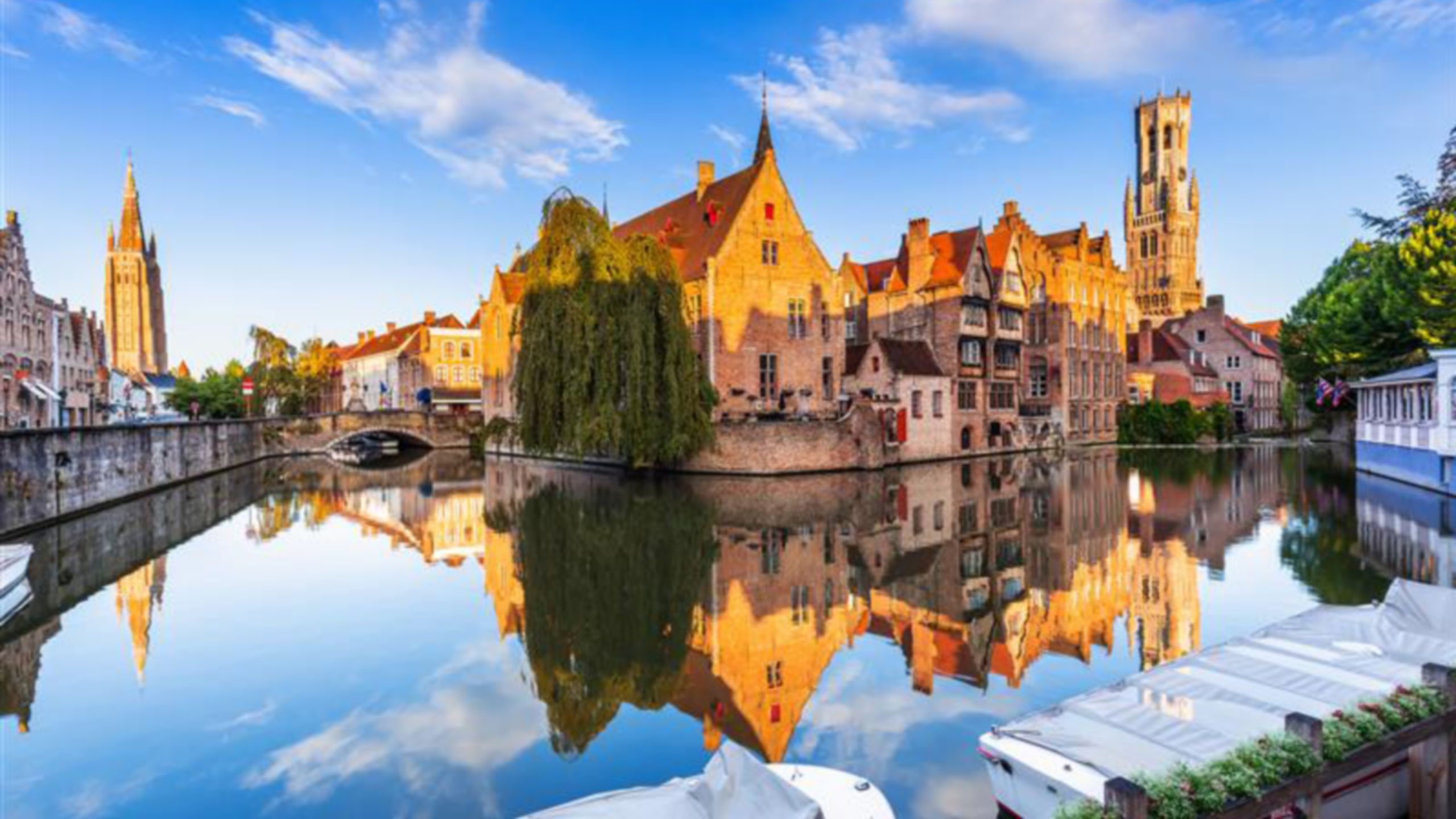 El campanario de Brujas reflejado en las aguas de un canal en Brujas, Bélgica