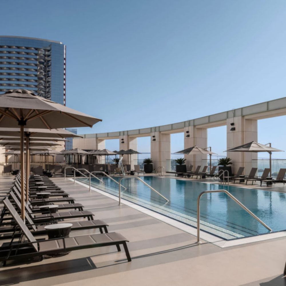 A rooftop swimming pool surrounded by lounge chairs and large umbrellas on an elevated terrace