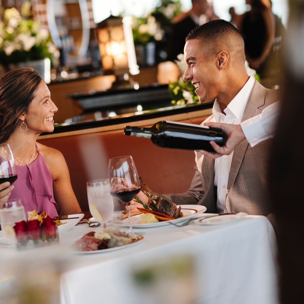 A Cast Member pours wine into the glasses of a couple dining at Palo