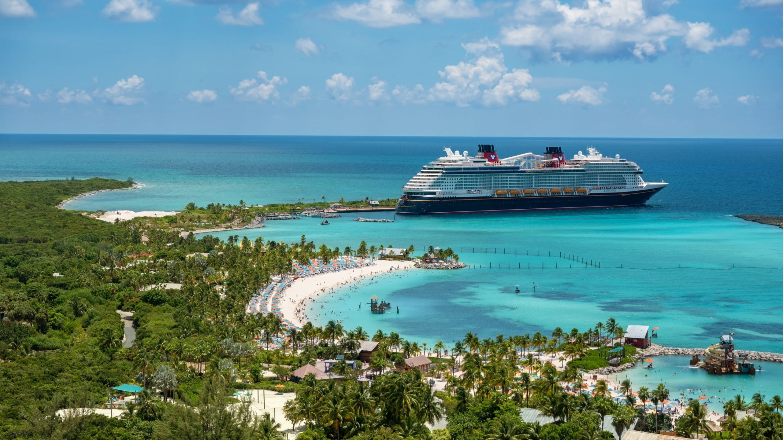 A Disney Cruise Line ship docked at Disney Castaway Cay surrounded by calm waters and sandy beaches lined with palm trees