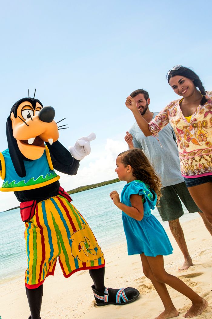 Pateta usando uma roupa de Junkanoo dançando com uma família de 4 pessoas na praia
