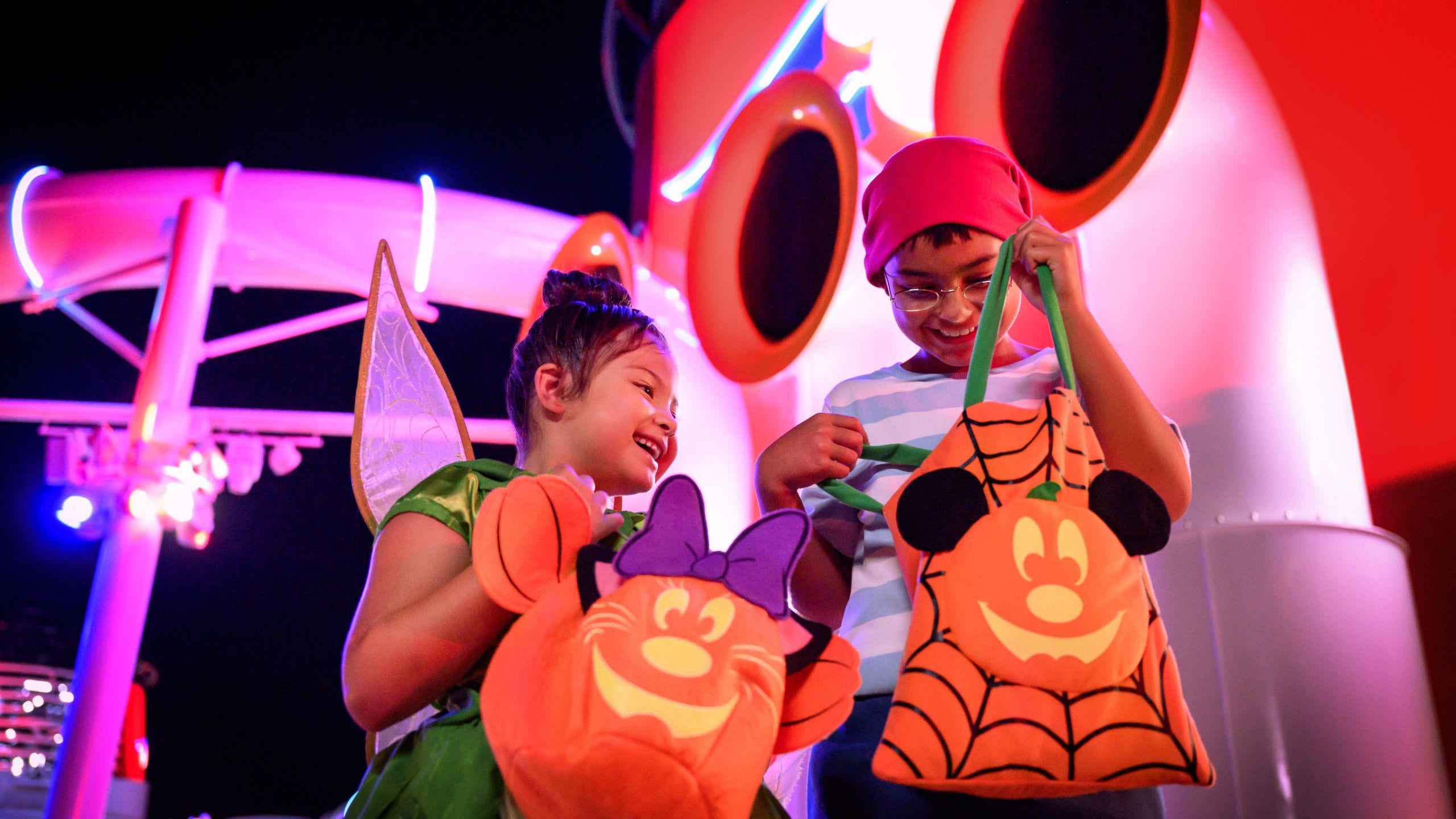A girl dressed as Tinker Bell and a boy dressed as Smee holding Mickey Mouse Halloween treat bags aboard a Disney cruise ship
