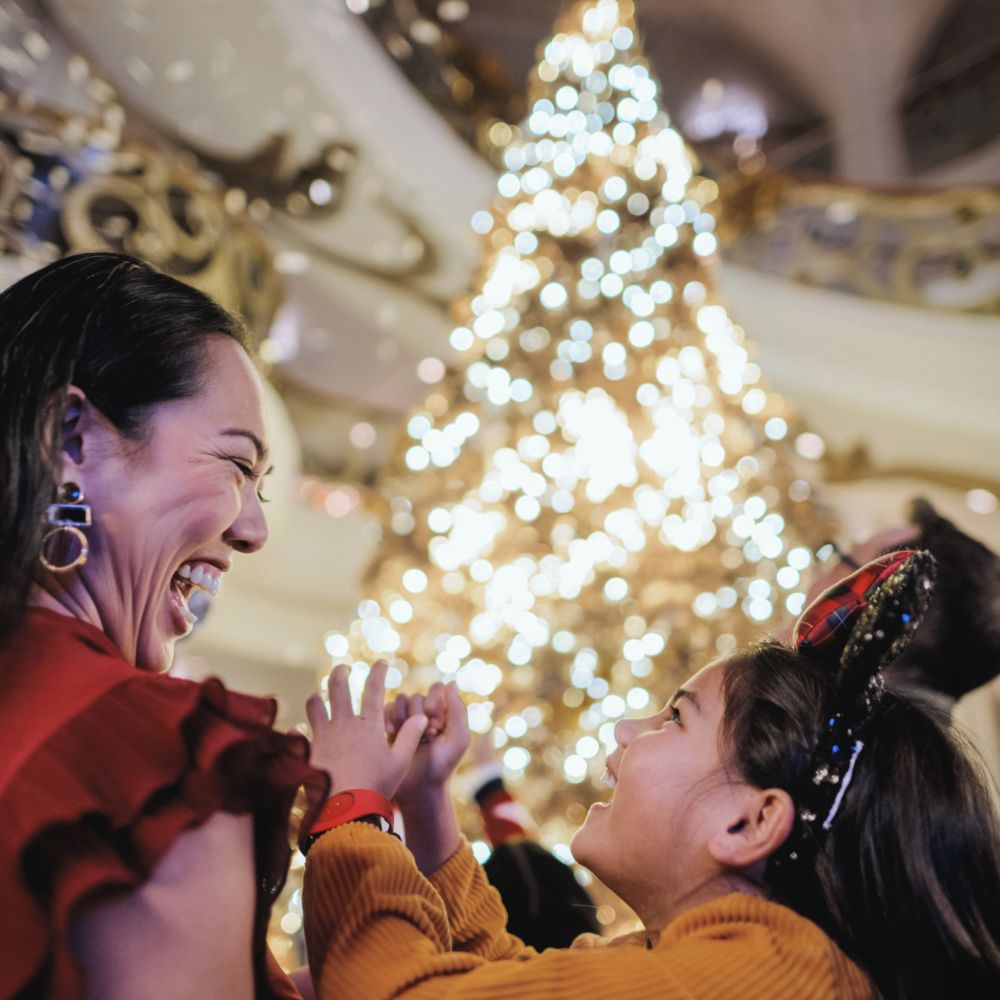 A mother and daughter laughing together in front of an illuminated Christmas tree