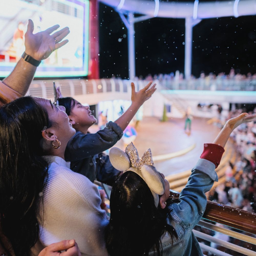 A family reaching out towards imitation snow flurries falling during    a holiday show on a Disney cruise ship