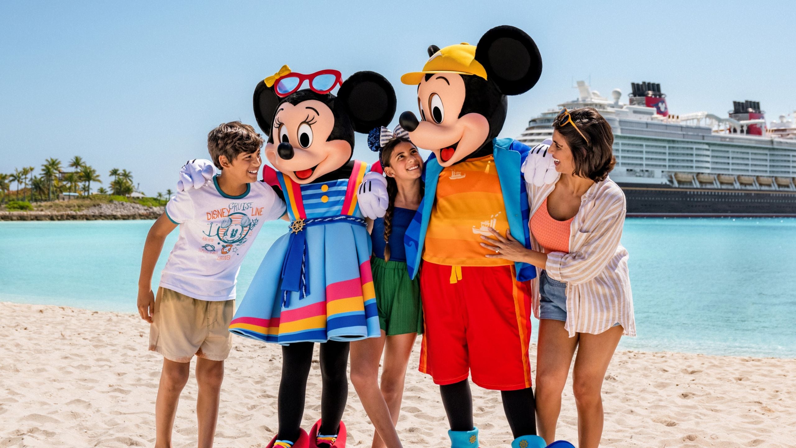 Mickey Mouse and Minnie Mouse greeting Guests on a beach with a docked Disney Cruise Line ship