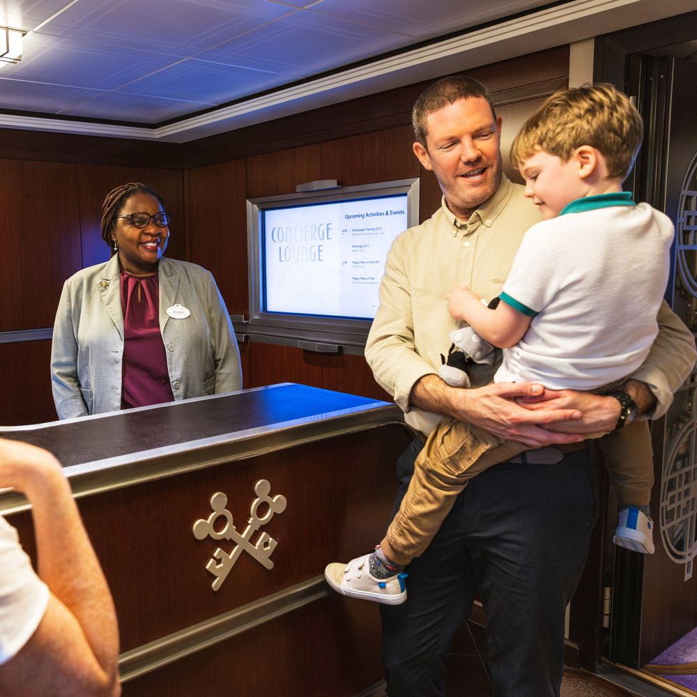 A father holding his son in his arms and a Cast Member at a Concierge desk