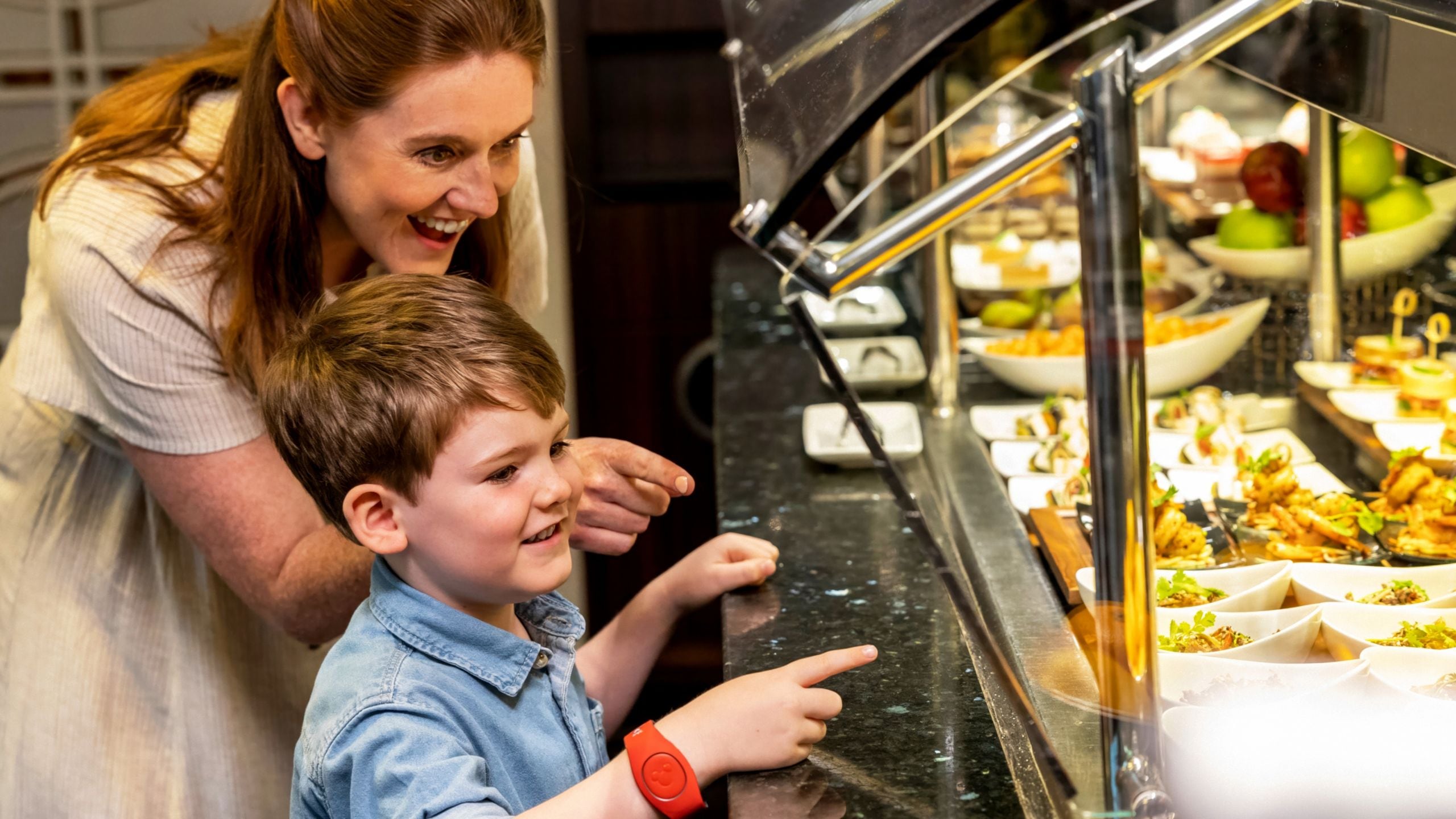 A woman and a young boy pointing at items at a buffet