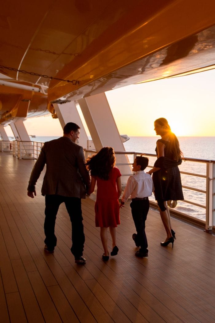 Uma família de 4 pessoas caminhando ao longo do deck de um navio da Disney Cruise Line ao pôr do sol