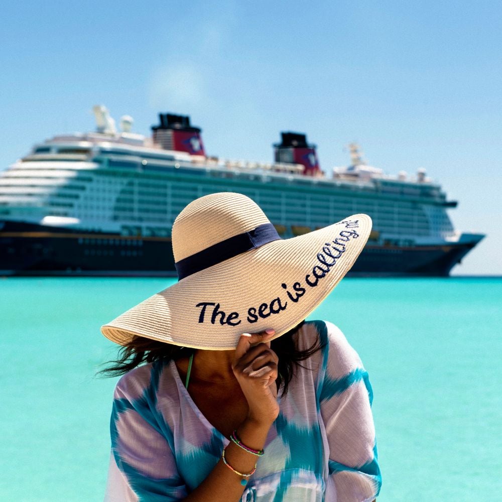 Uma mulher cobre o rosto com um chapéu em frente ao navio de cruzeiro Disney Dream