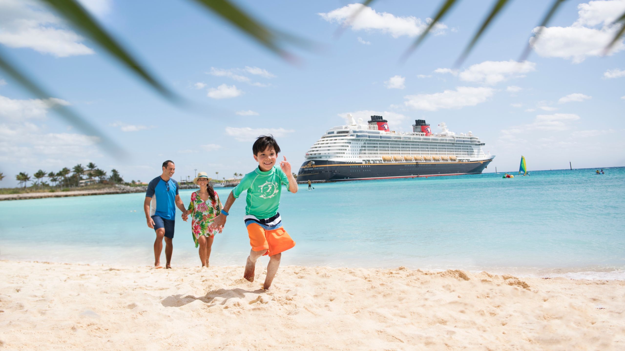 Uma criança corre na praia na frente de seus pais com o navio Disney Fantasy atracado atrás deles