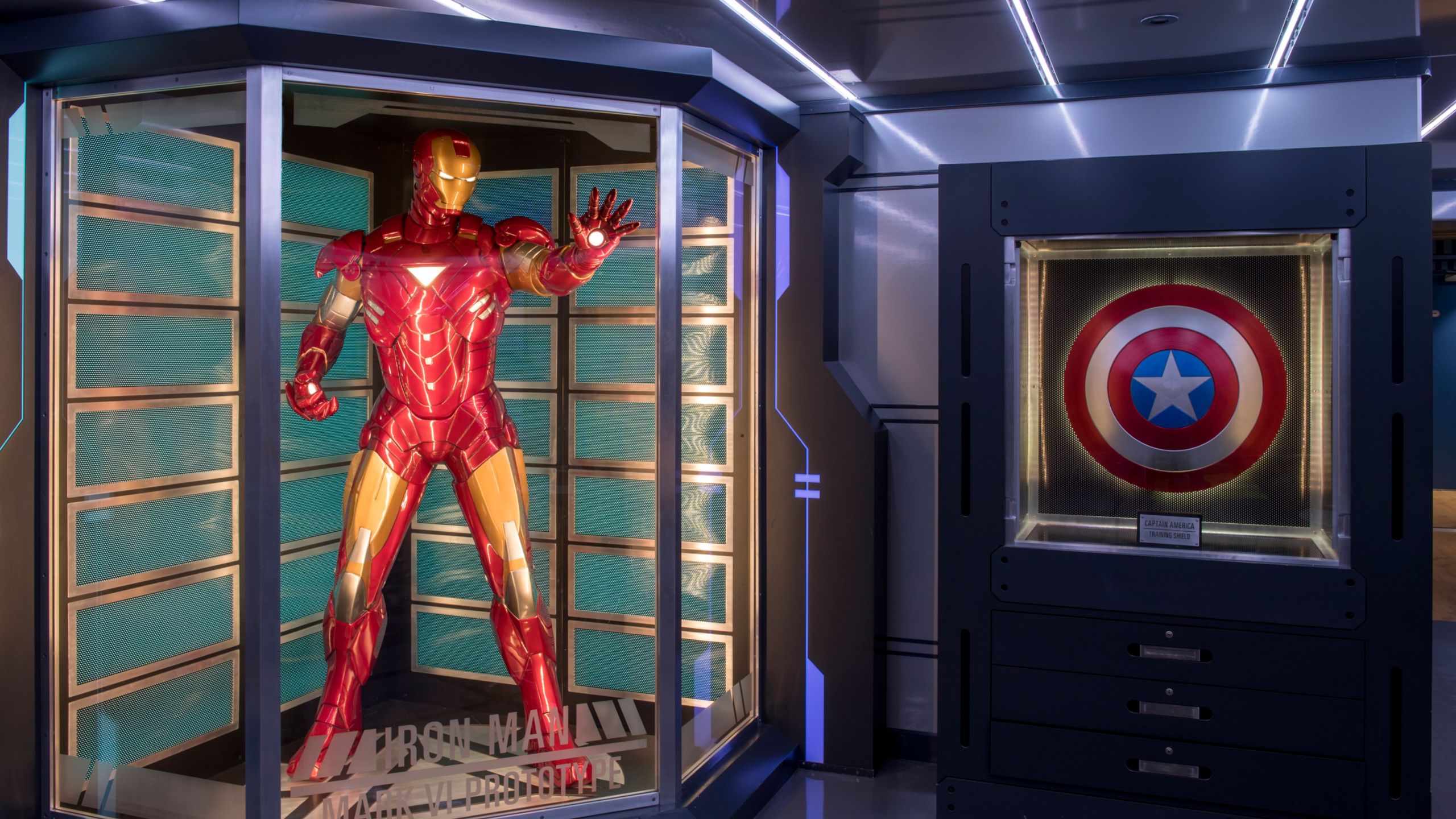 Traje do Homem de Ferro protegido por um vidro ao lado do escudo do Capitão América 