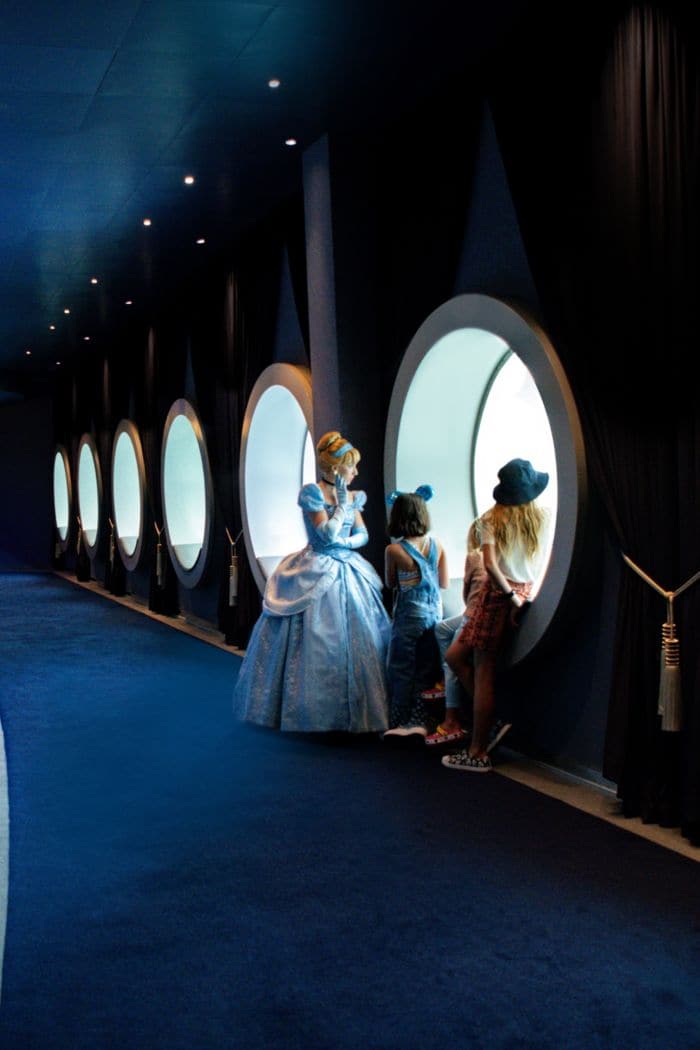Cinderella looks through round windows with children aboard a Disney Cruise Line ship