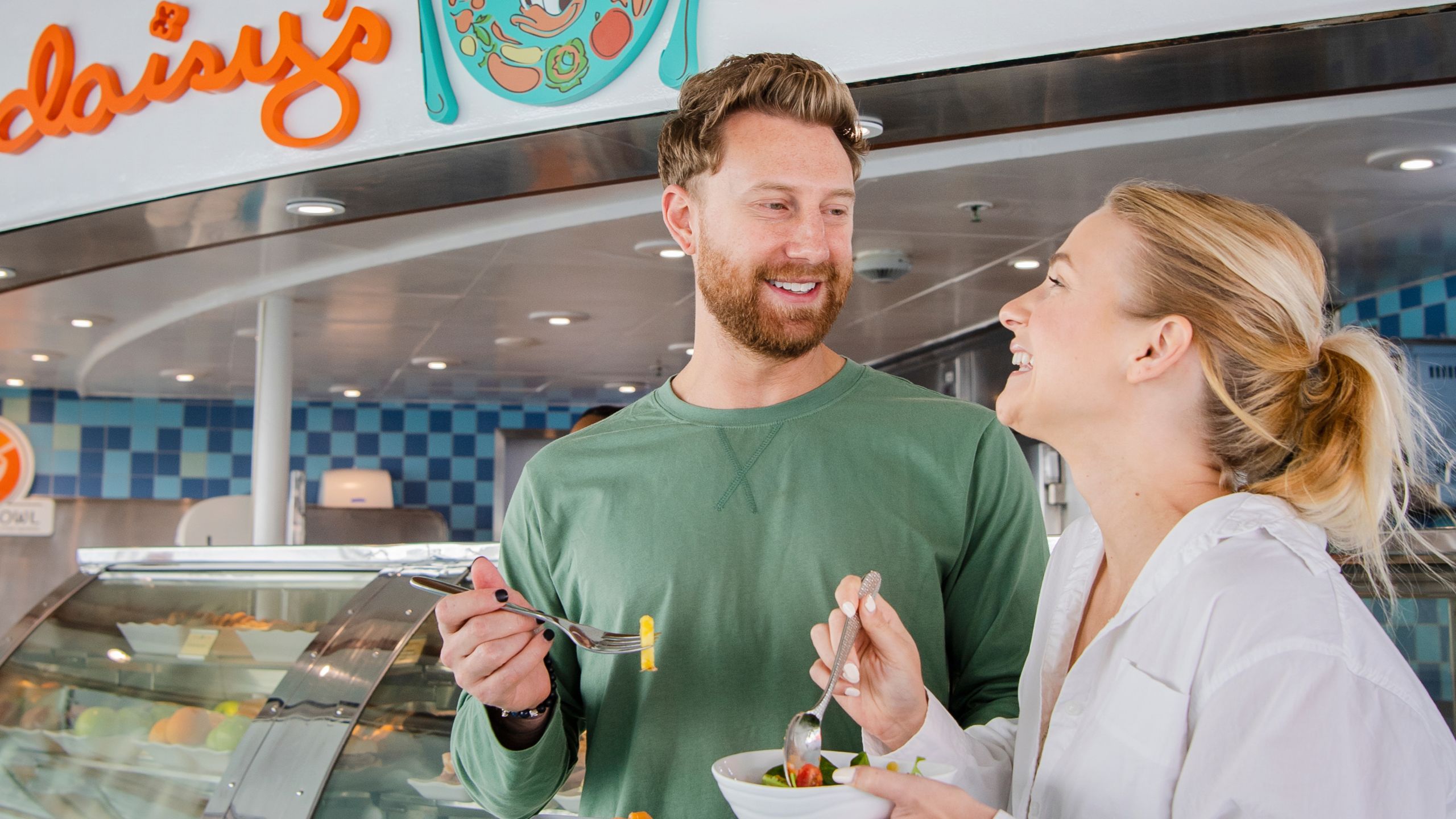 A man and woman smile and eat salad in front of Daisy's De Lites