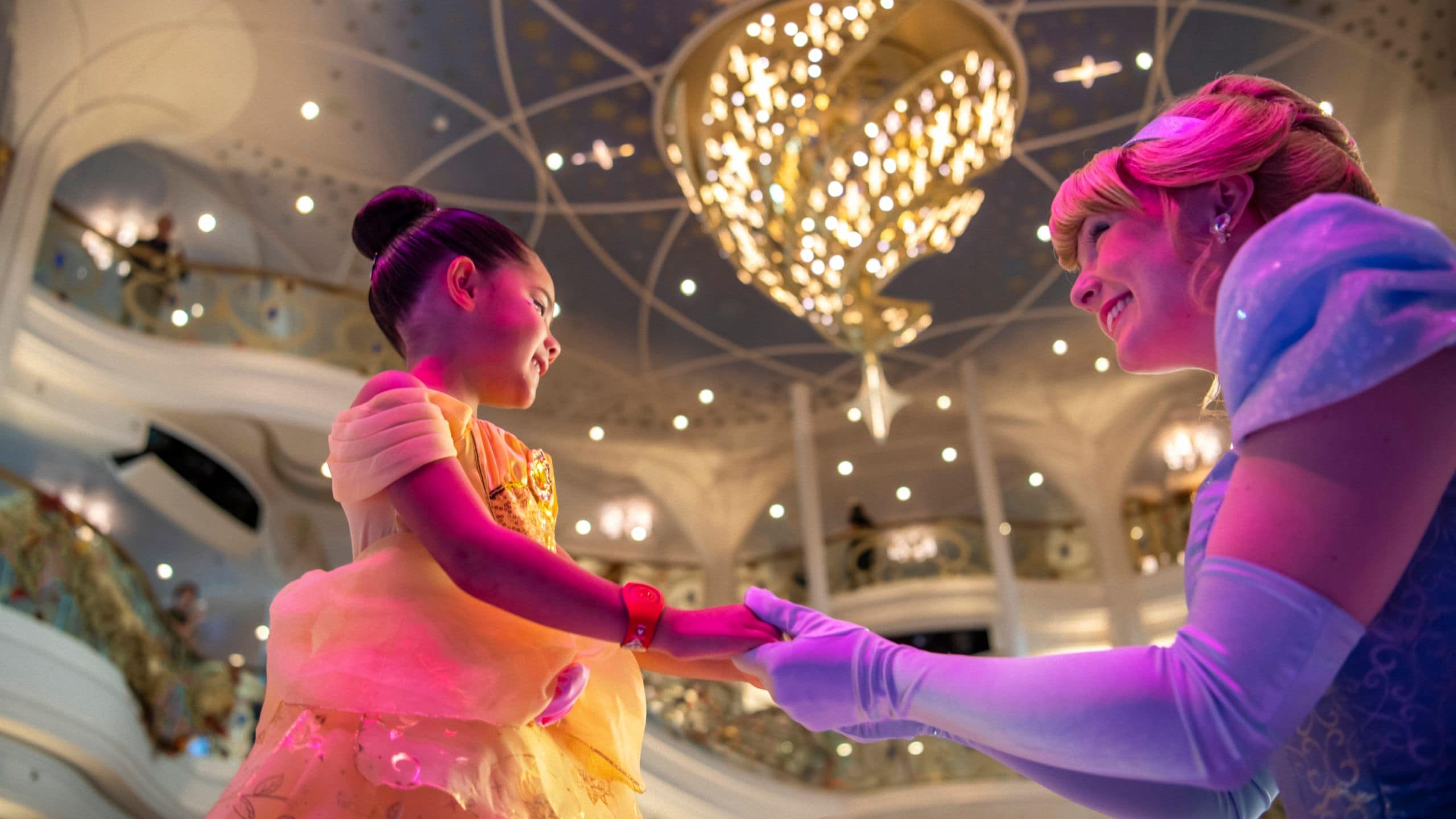 Uma garotinha vestida de Princesa Belle de mãos dadas com Cinderela