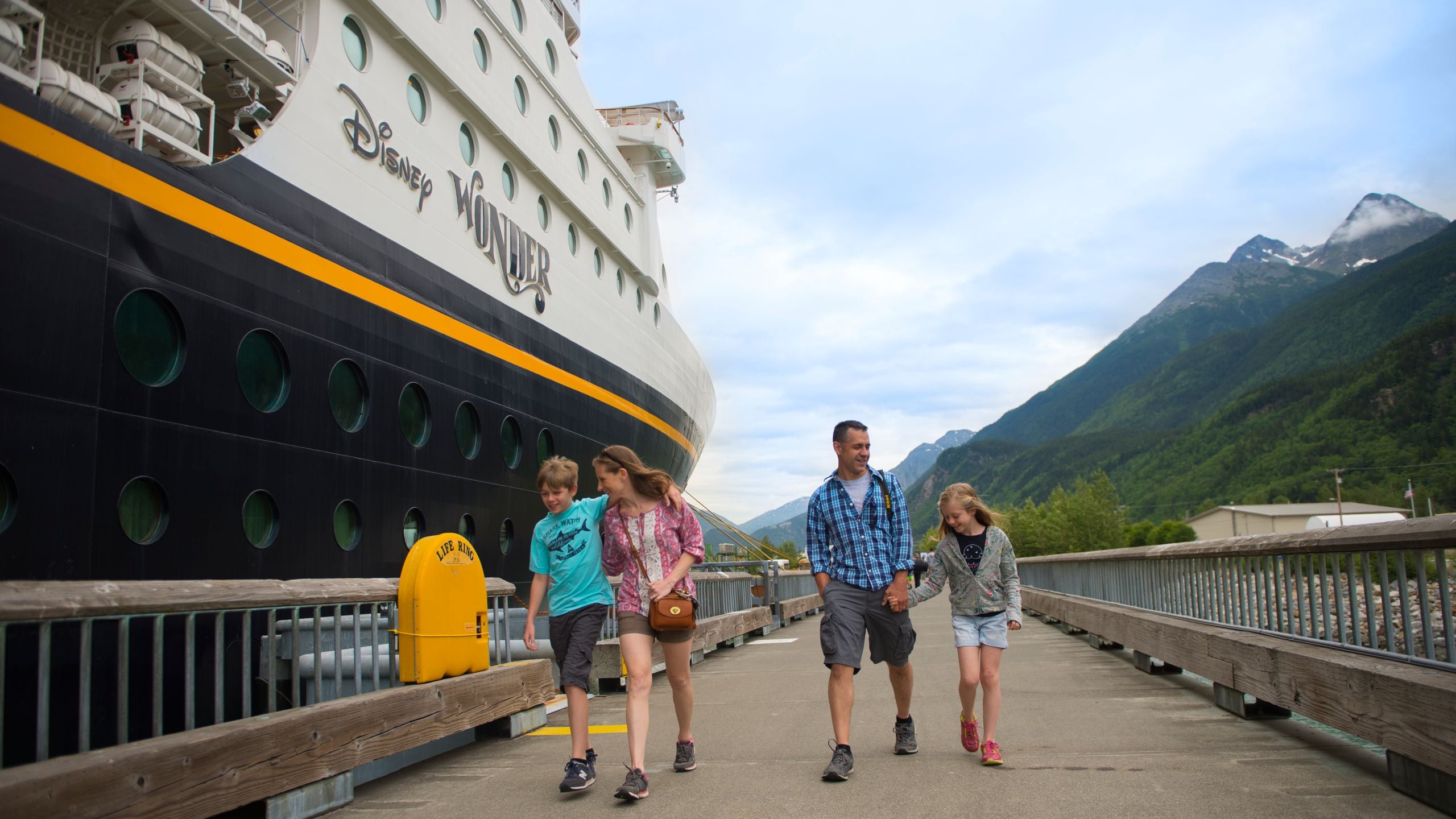 Uma família caminhando em um cais junto ao navio de cruzeiro Disney Wonder
