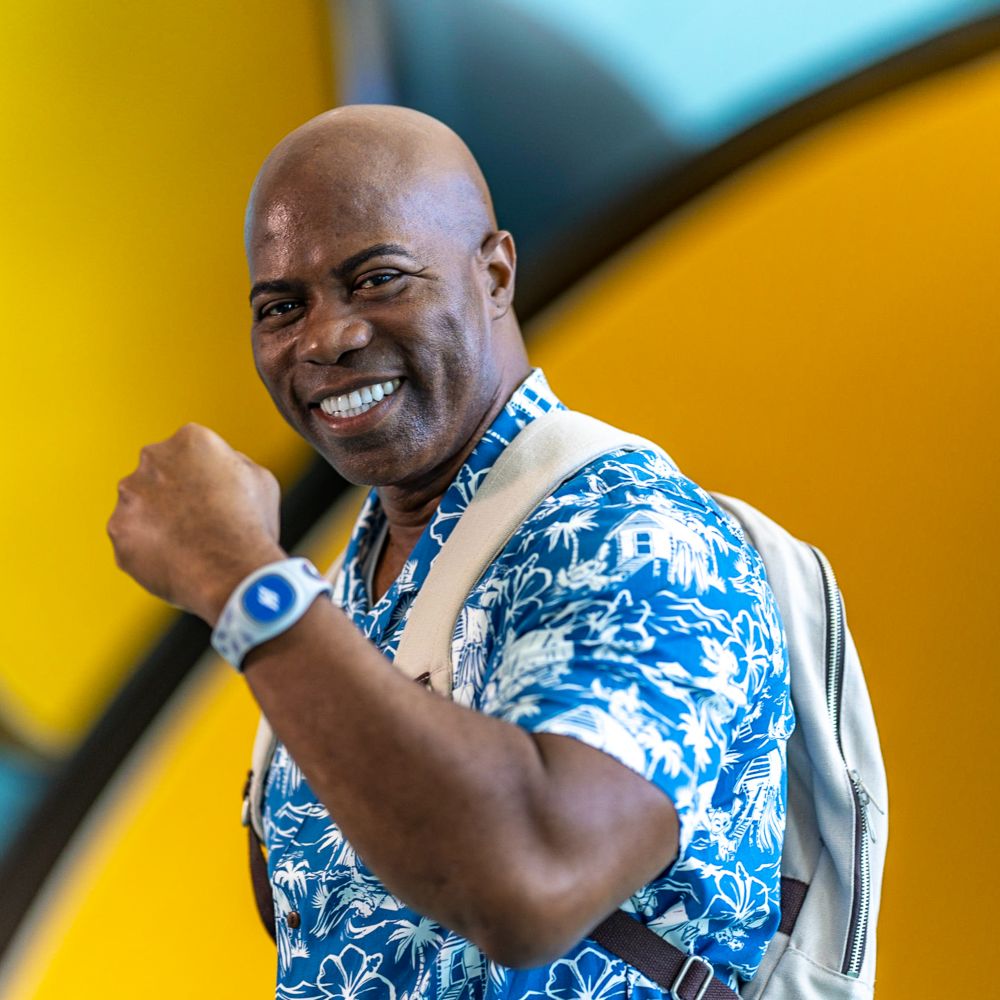 A man smiles while raising his arm up to show off his Disney Band Plus