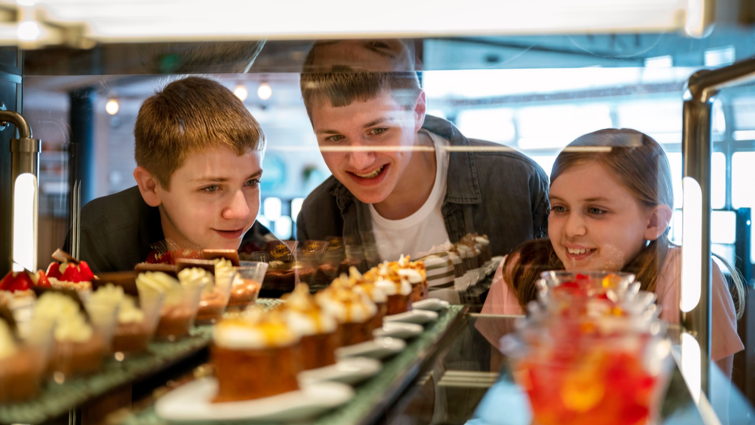 Three teenagers looking at a case filled with desserts