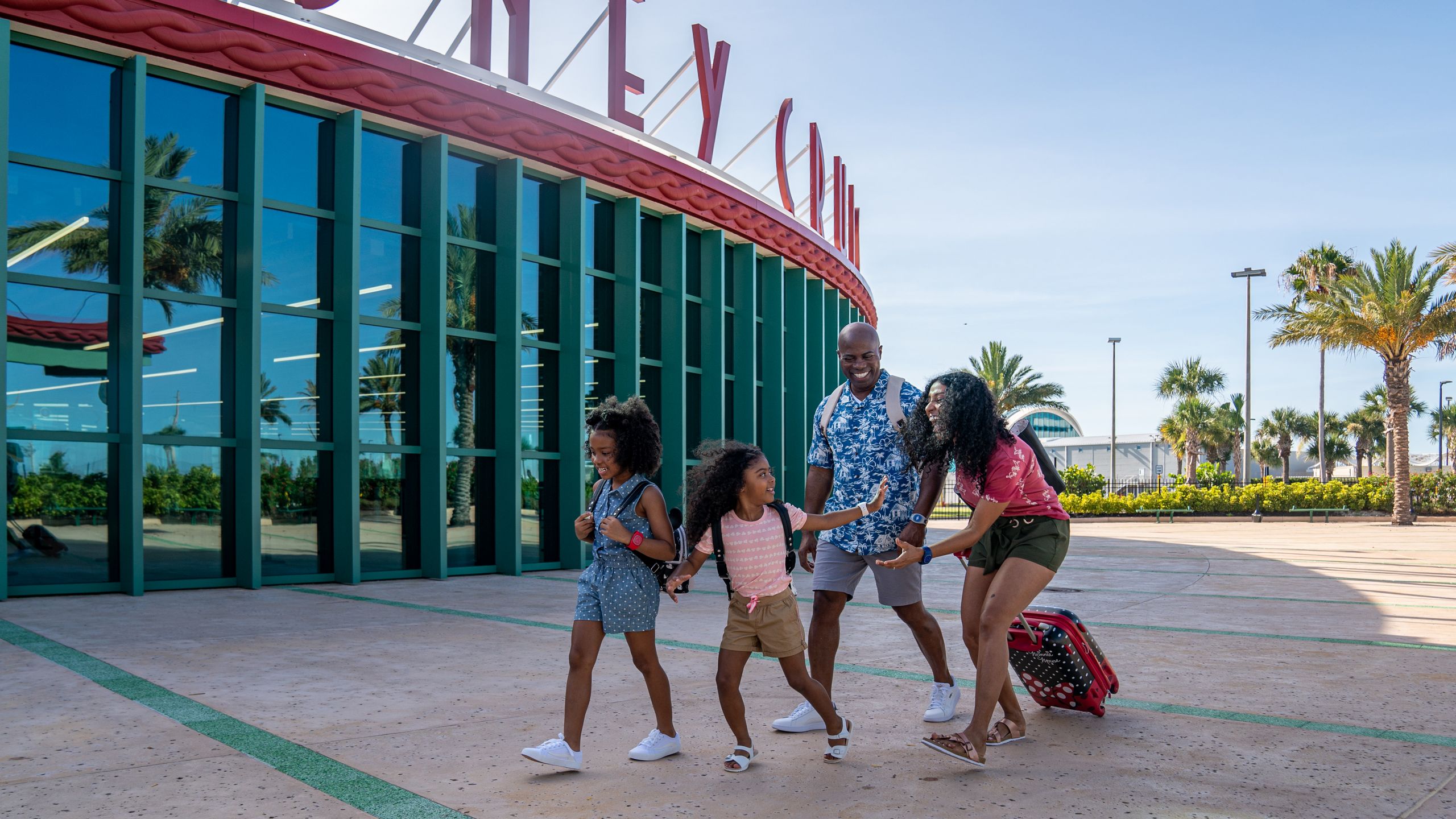 Two parents and 2 young girls walking in front of a Disney Cruise Line terminal