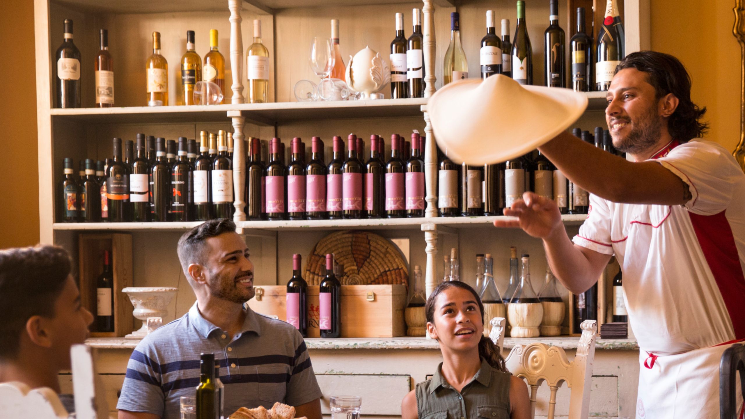 A man, a boy and a girl sitting at a dining table, watching a chef spin pizza dough