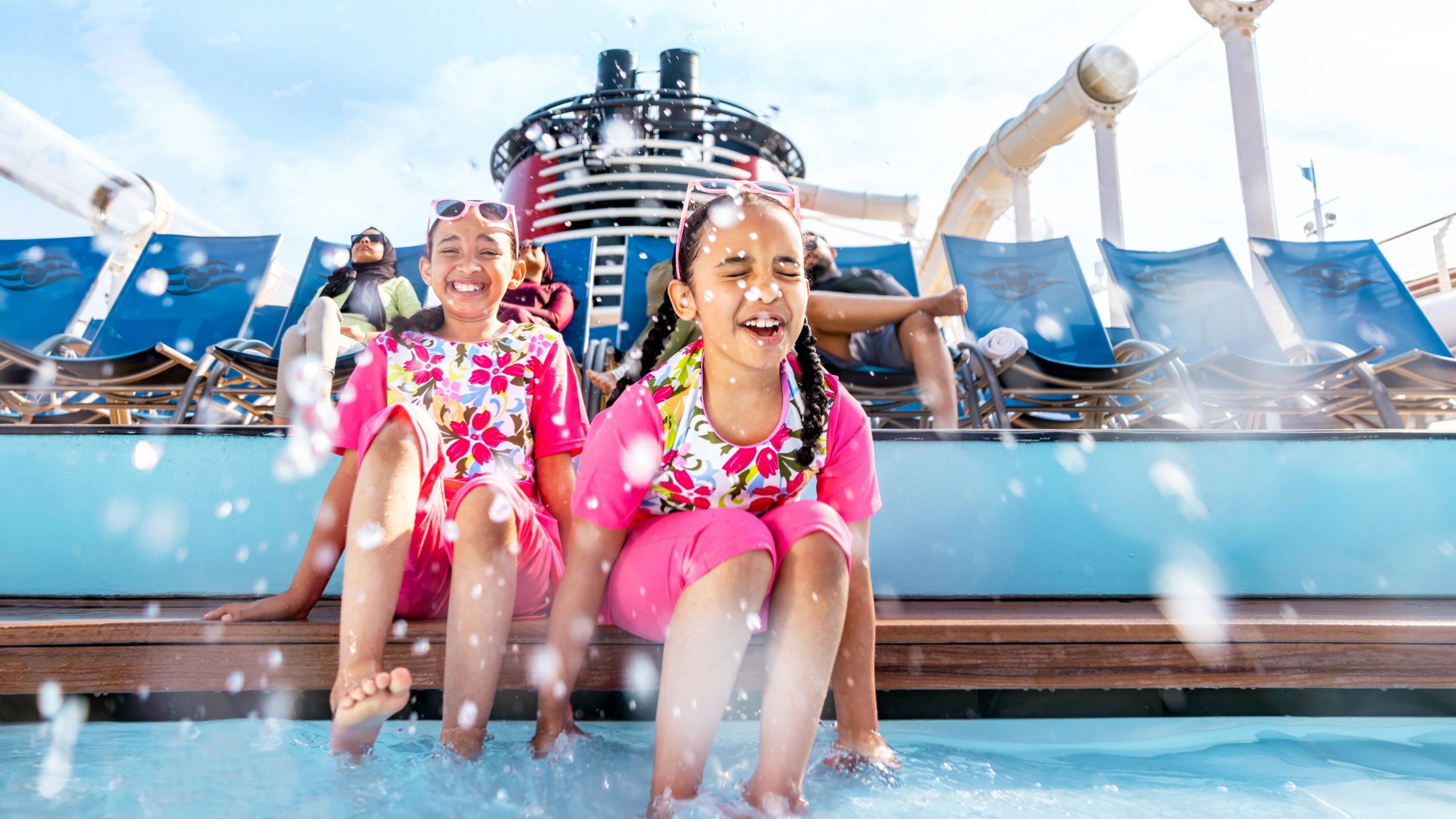 Two young girls splash water as they sit with their feet dipped into a pool