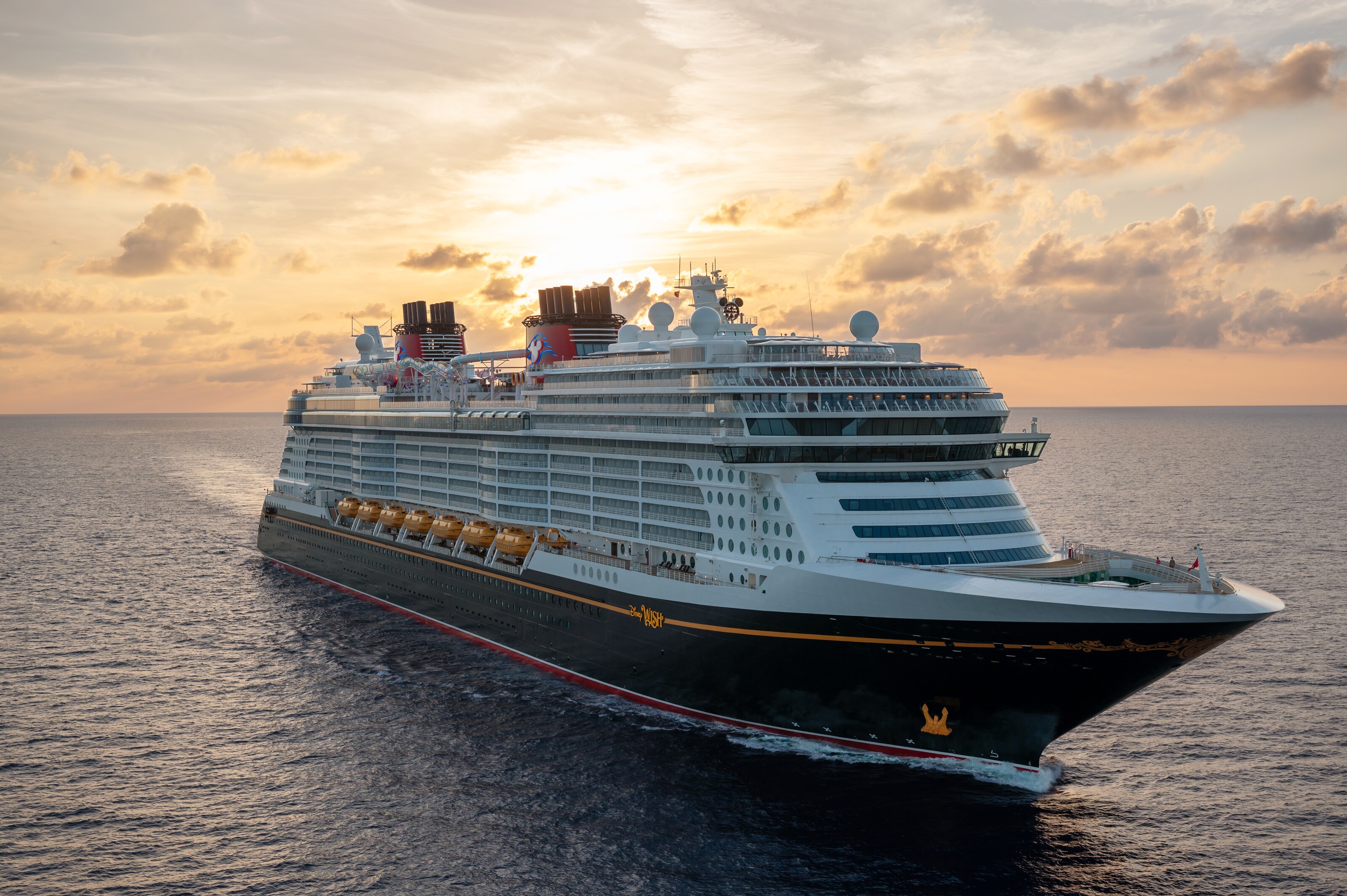 The Disney Wish sailing along the ocean with the sun low on the horizon