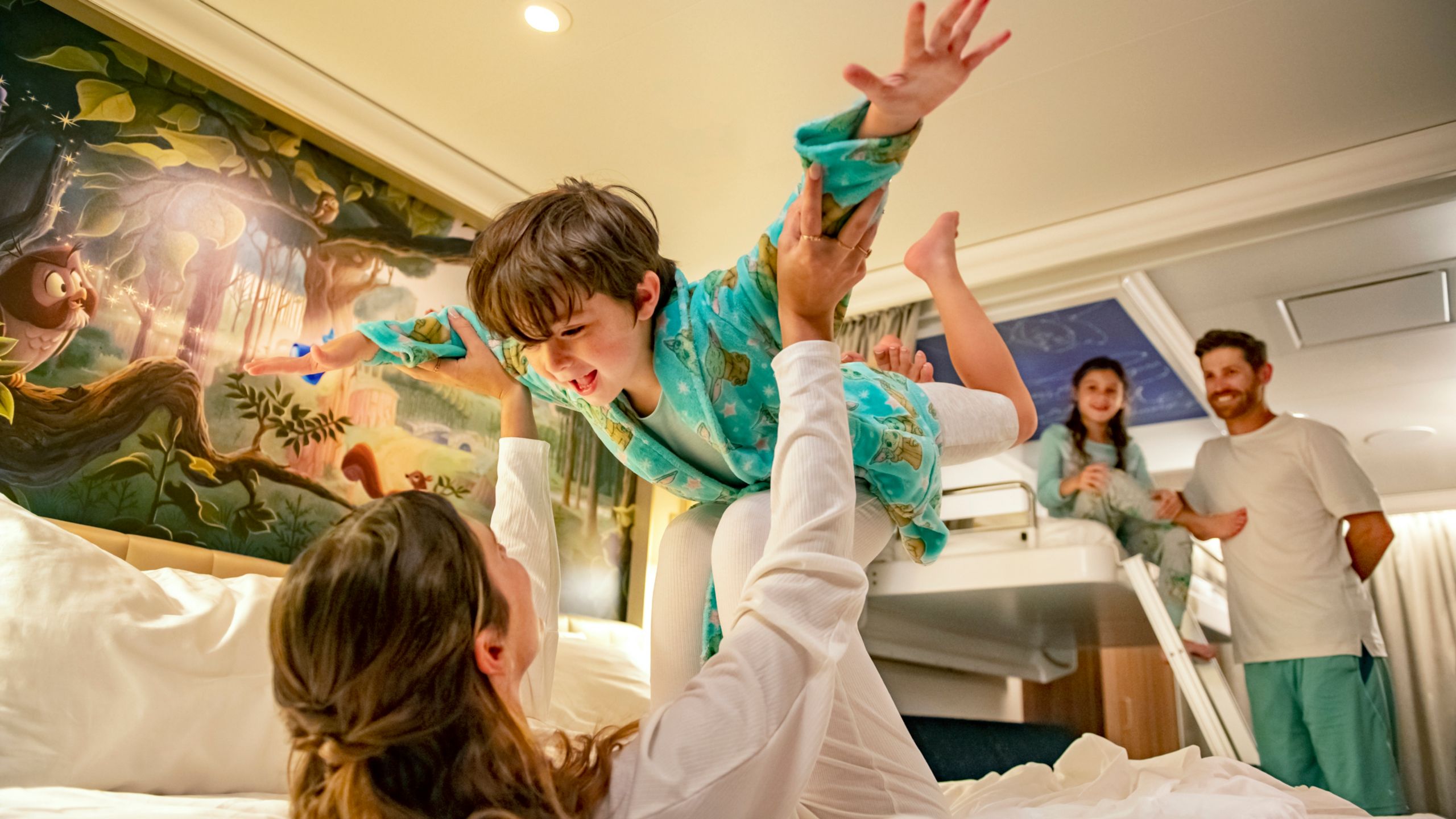 Una madre en una cama con su hijo pequeño en las piernas, mientras el padre y la hija miran desde la litera en un camarote de Disney Cruise Line