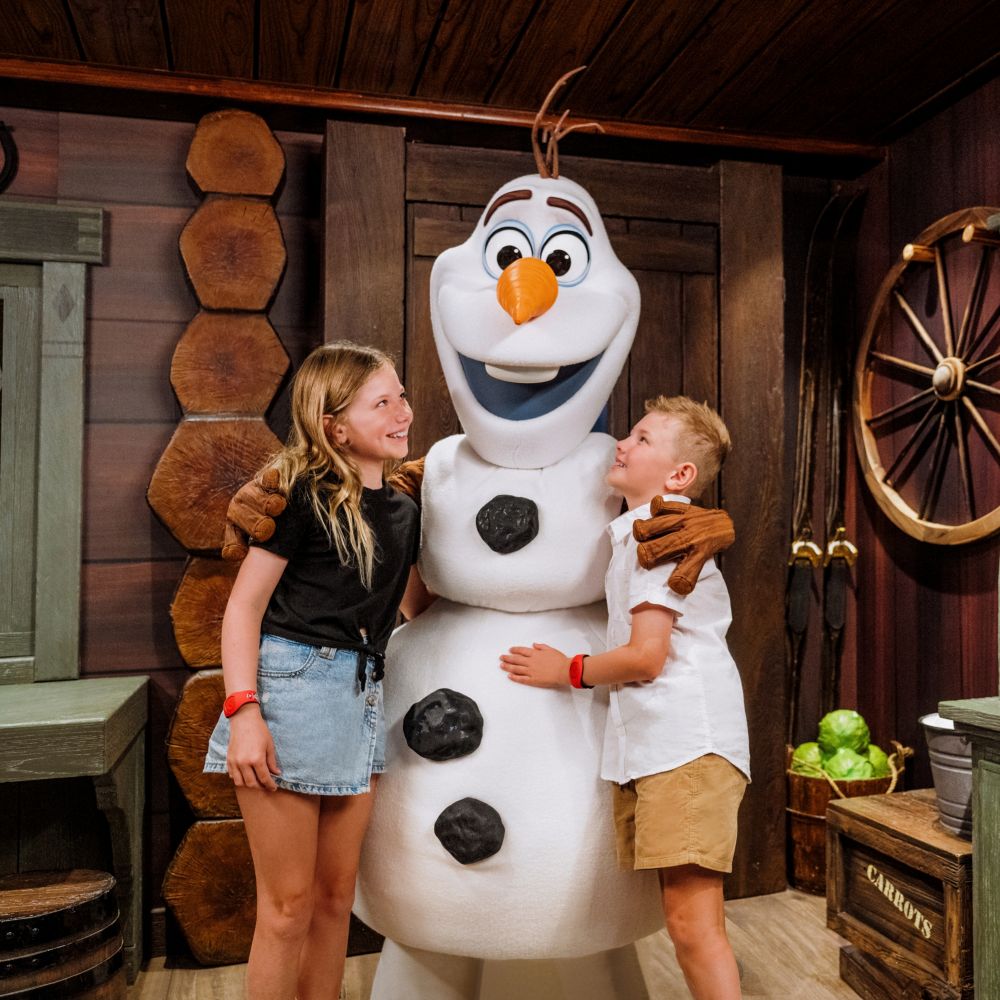 Una niña y un niño posando con Olaf, el muñeco de nieve