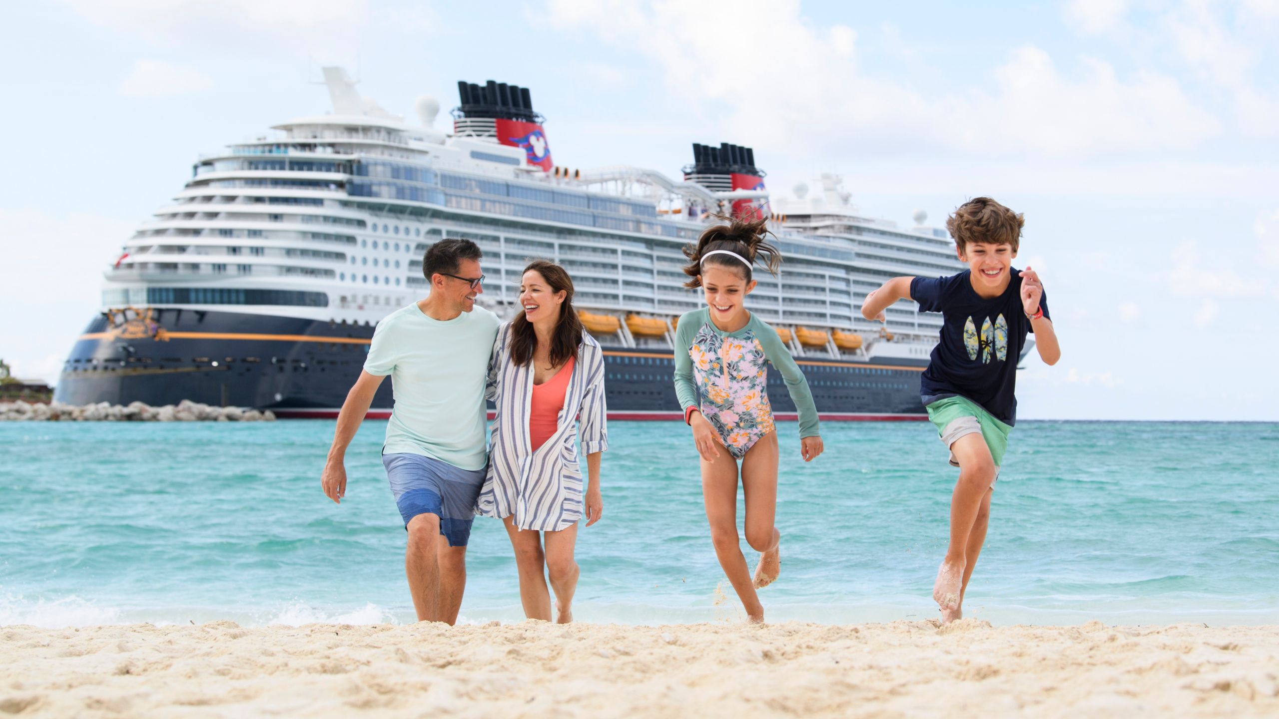 A family walking along a beach near a Disney Cruise Line ship