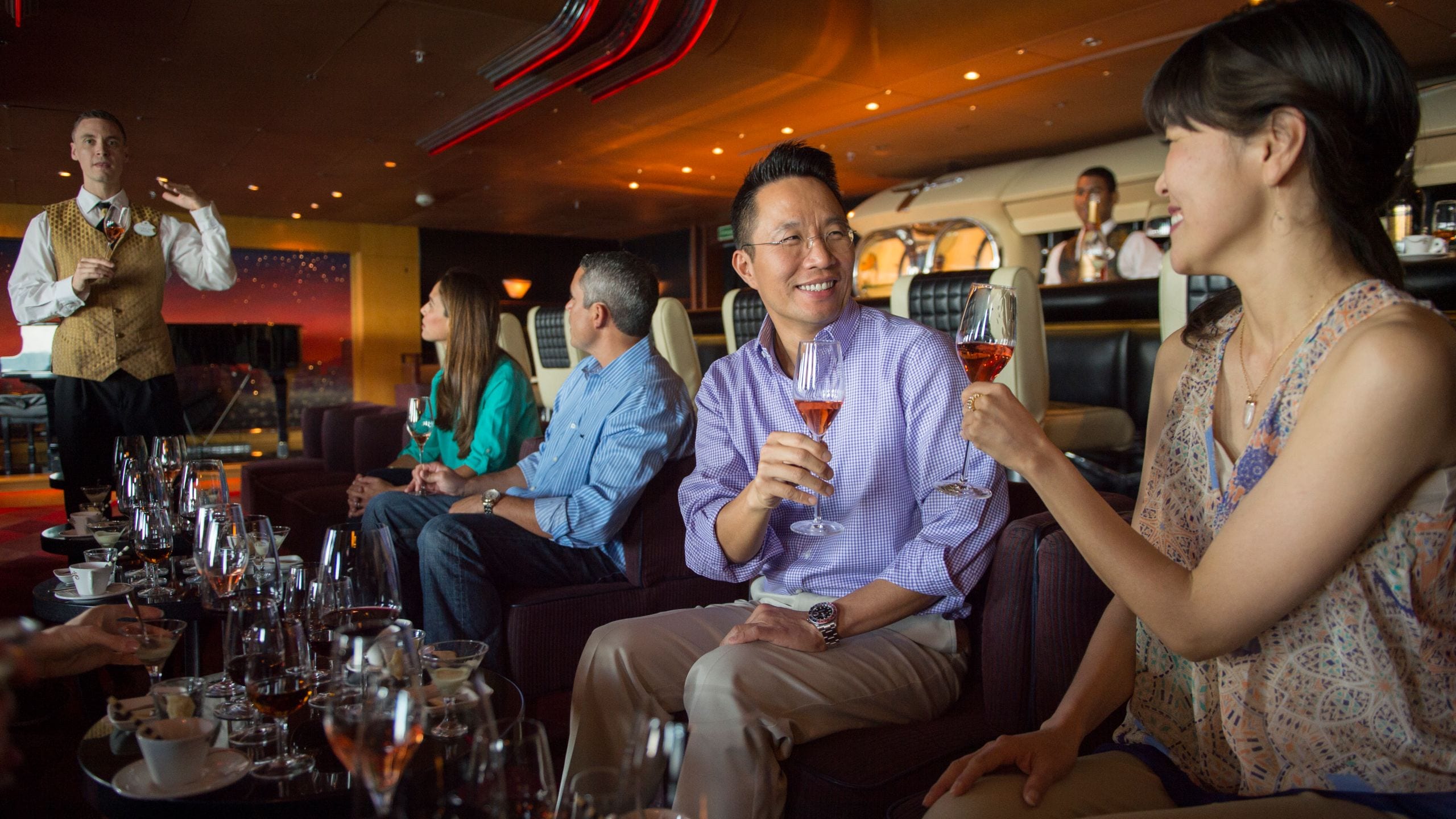 A Cast Member speaking to a table of Guests, while 2 of the Guests toast each other