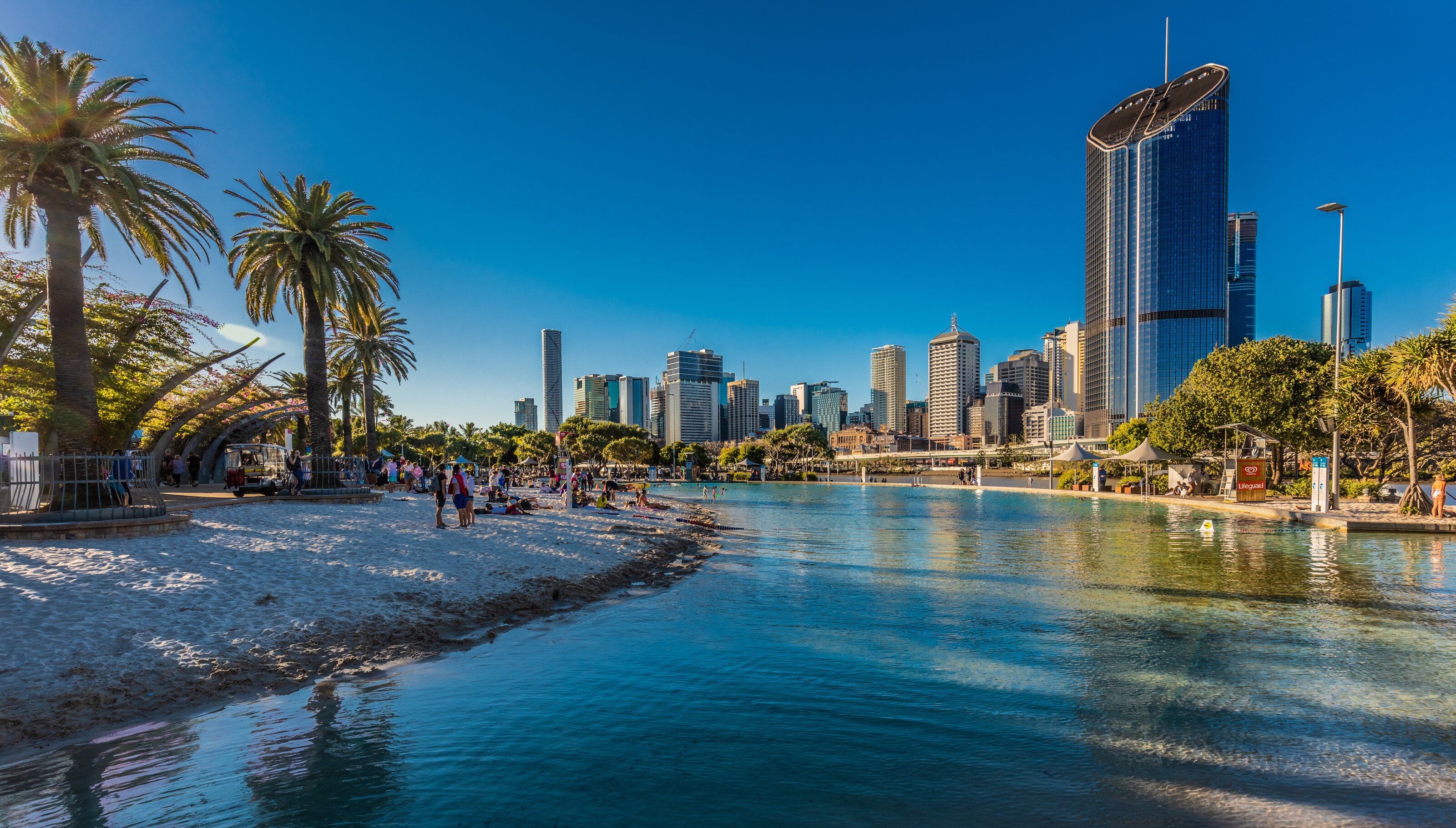 A tranquil river with a tropical beach on one side and a cosmopolitan city on the other