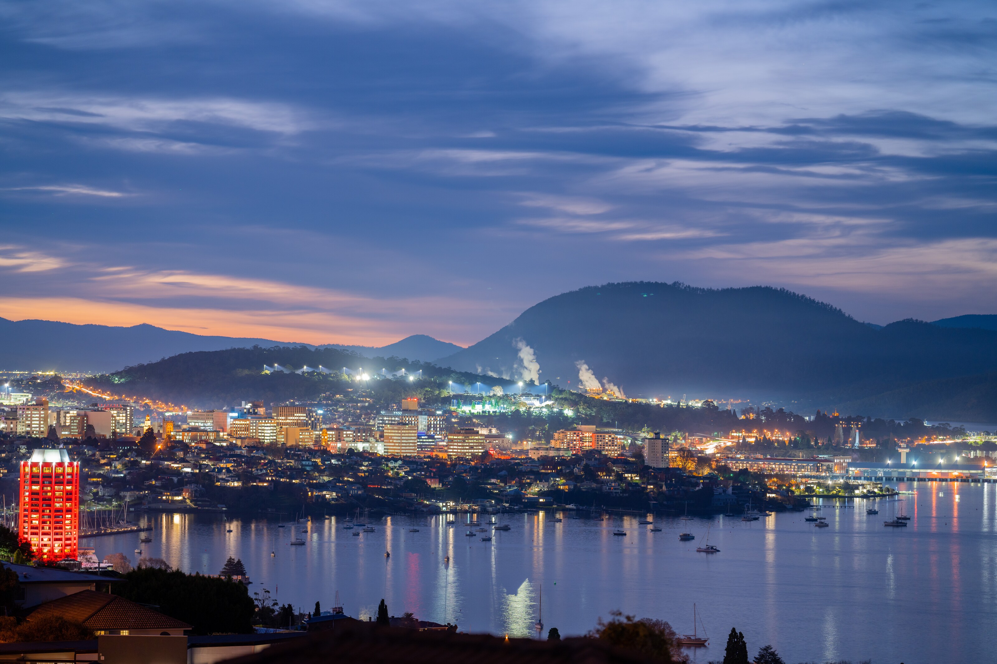 A coastal city surrounded by rolling hills and mountains at night