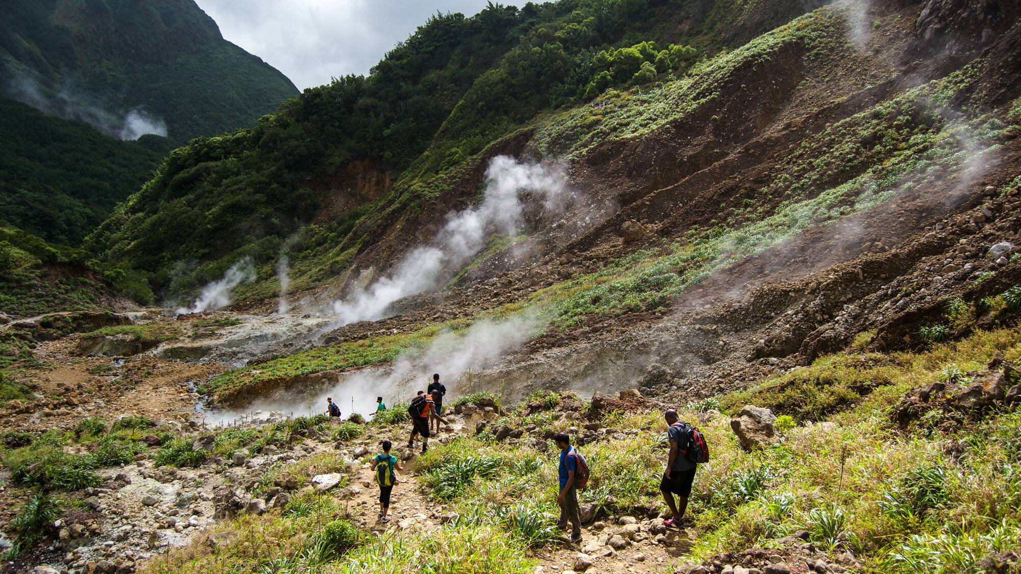 Steam rising from a volcanic vent near hikers on a grassy hillside in Dominica