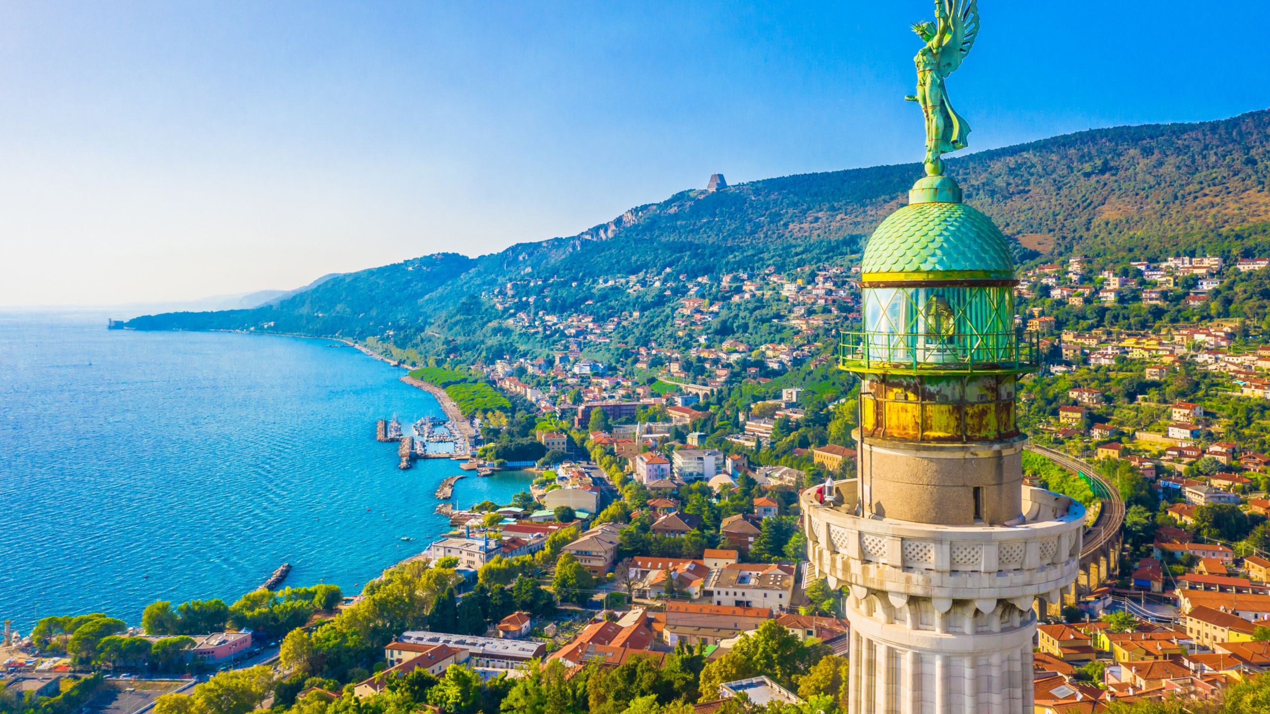 The statue Winged Victory tops the Faro della Vittoria lighthouse, looming over a hillside town on the Adriatic coast
