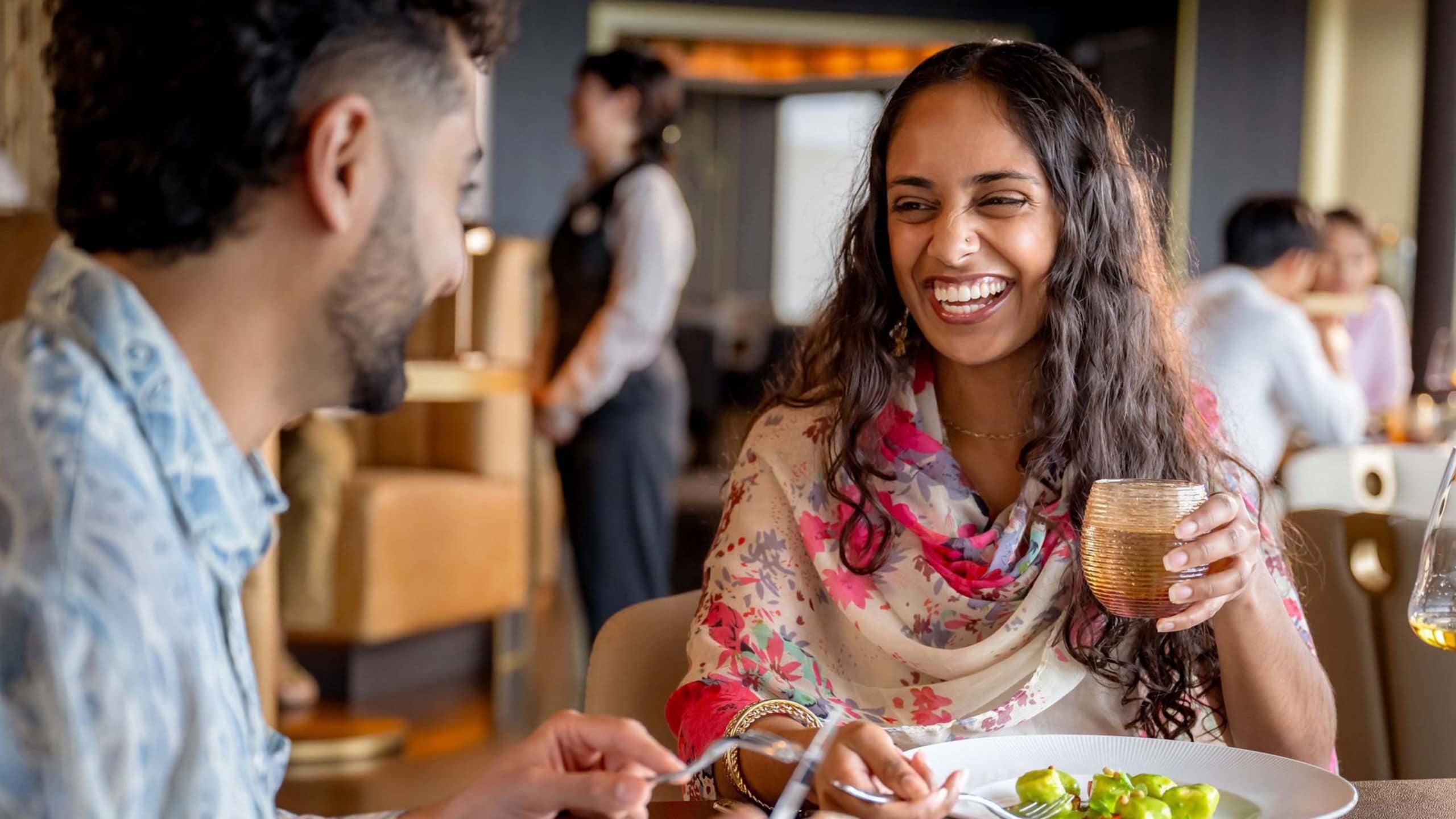 Uma mulher rindo e apreciando uma bebida ao lado de um homem comendo uma salada no Palo Trattoria a bordo do Disney Adventure