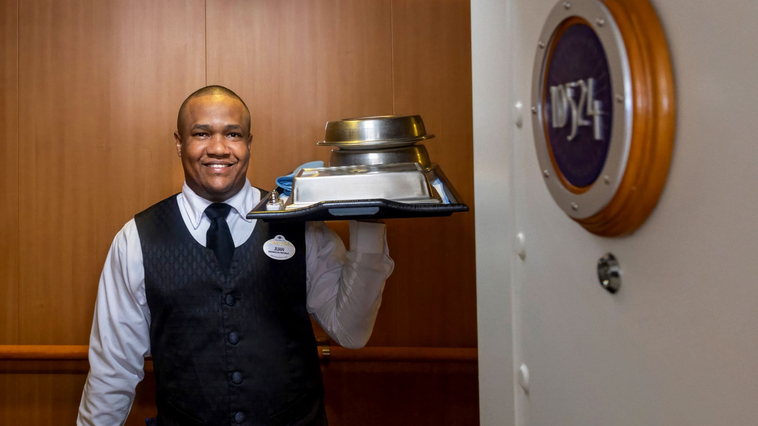 A cast member carrying a tray of dishes covered by metal cloches