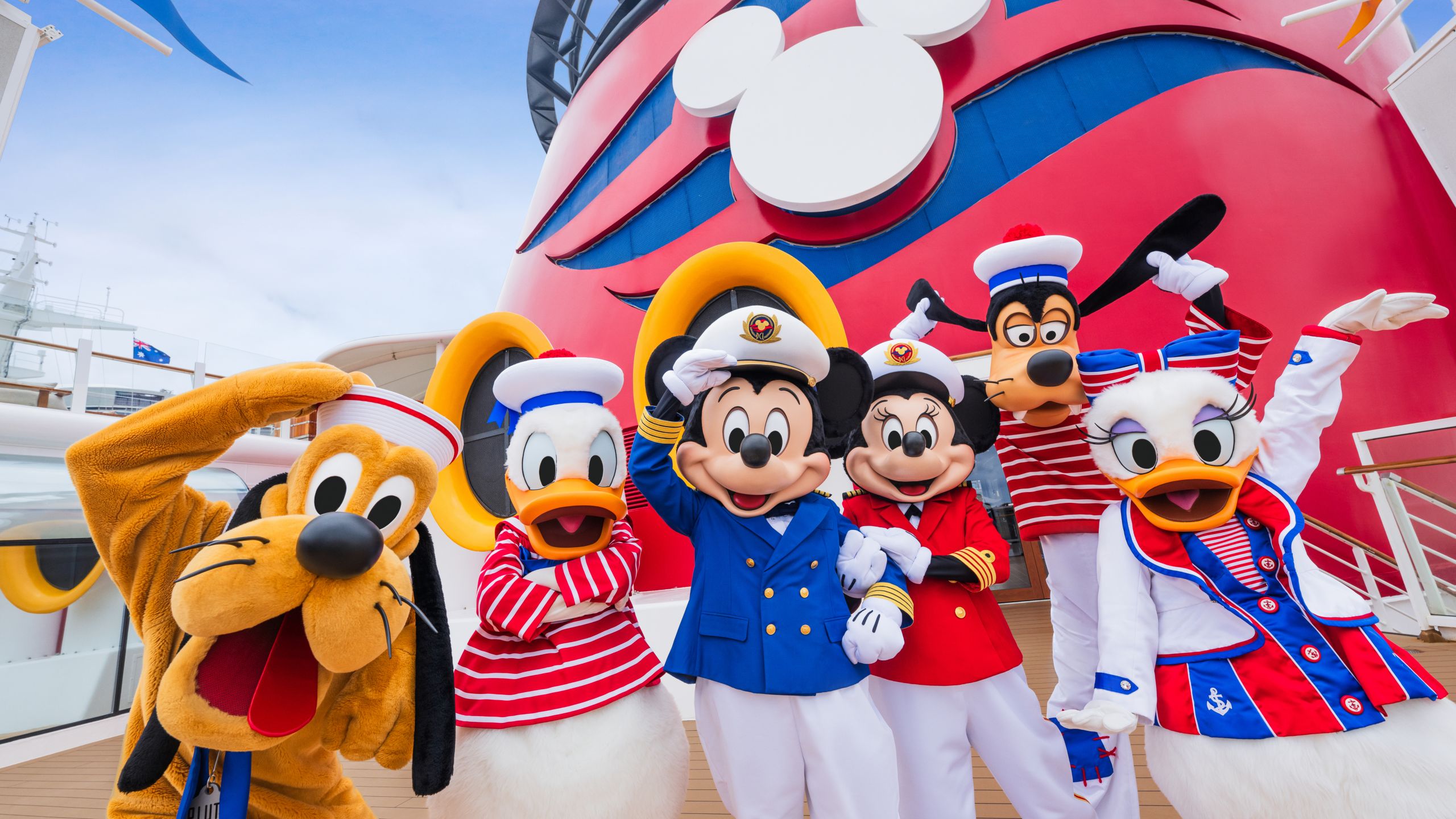 Mickey Mouse, Minnie Mouse and their Disney pals wave aboard the deck of a Disney Cruise Line ship