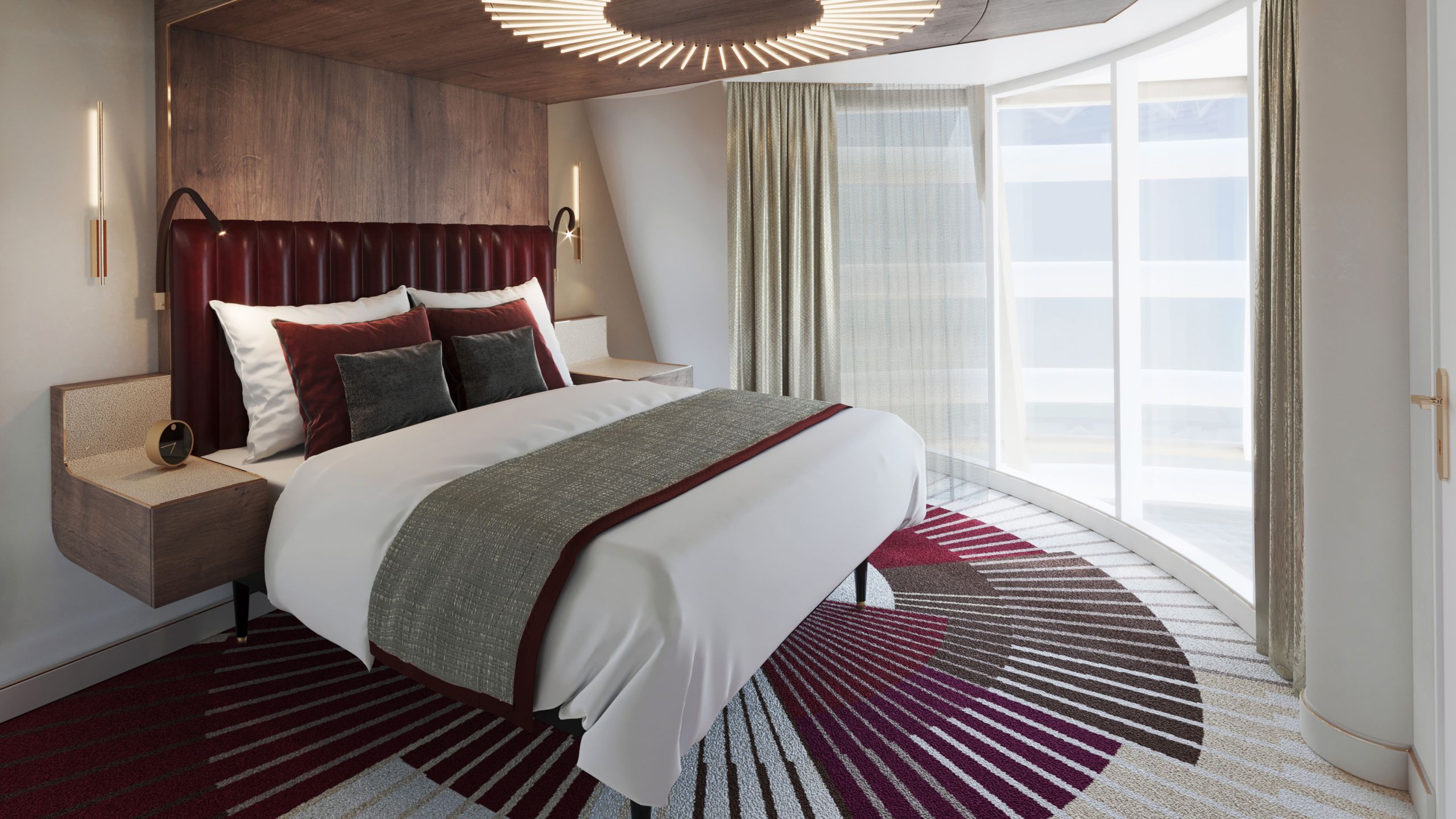 A queen size bed with a headboard that extends up the wall and across the ceiling, a circular overhead light and floor to ceiling ocean views