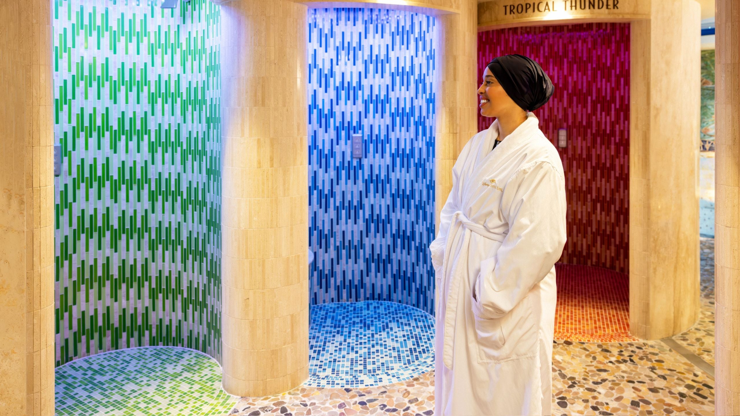 Uma mulher ao lado dos chuveiros vestindo um roupão de banho e um protetor de cabelo na Rainforest Room do Senses Spa