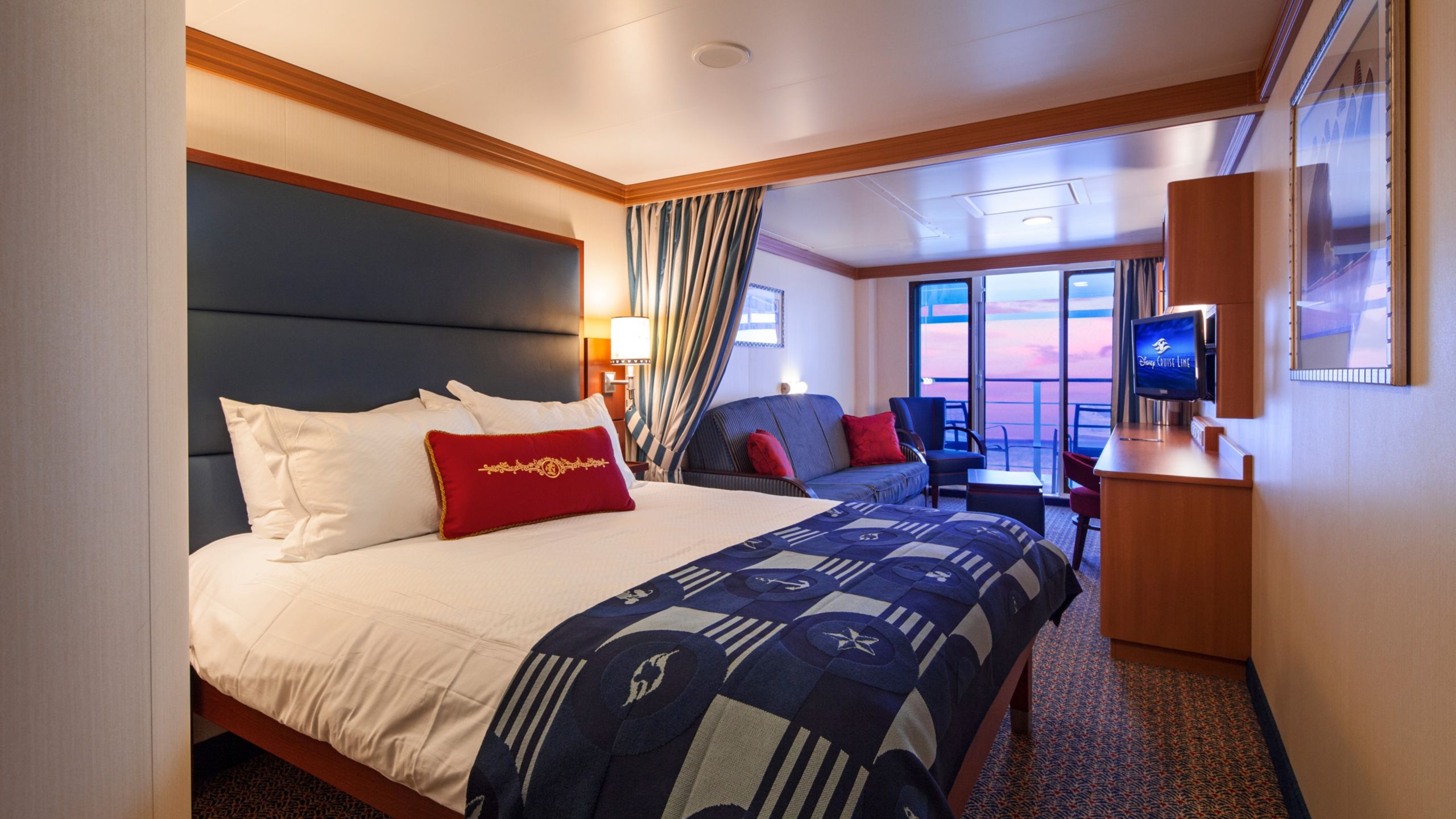 Uma cabine com uma cama queen size, sofá, mesa, TV e porta de vidro que leva para uma varanda 