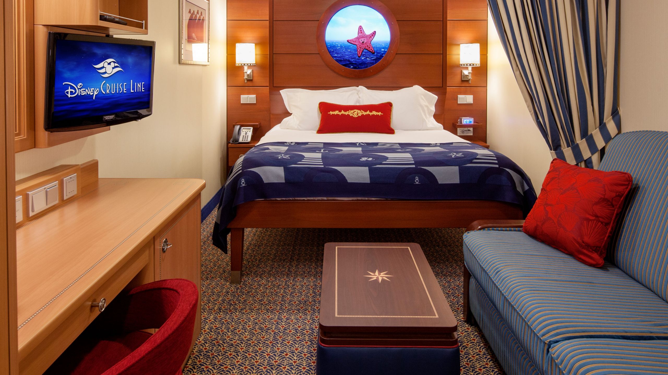 An inside stateroom with a sofa and a bed next to a ‘Magical Porthole’ screen showing views of the ocean in real time
