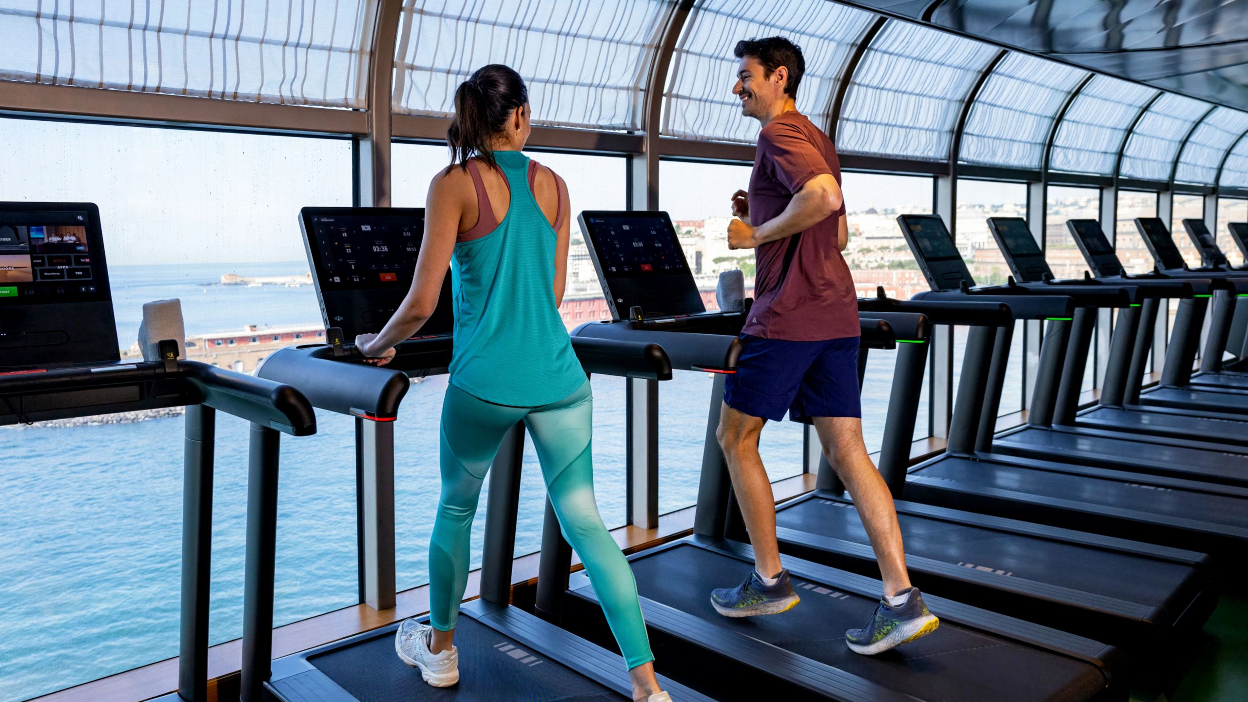 A woman and man chatting while walking on treadmills inside a fitness center