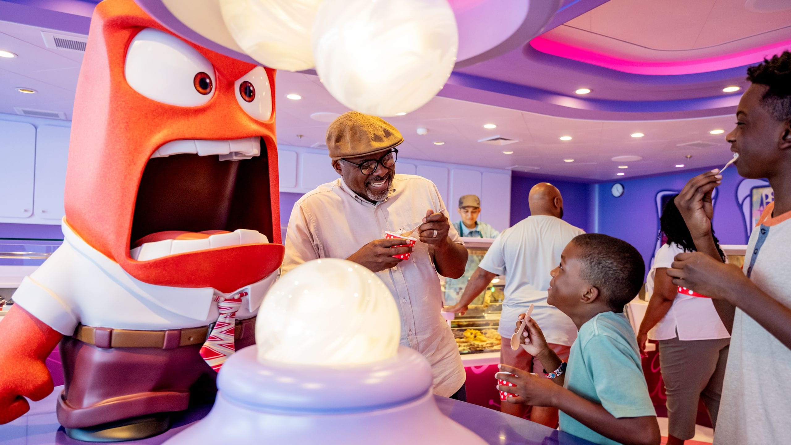 A family eating ice cream next to a statue of Anger at the Inside Out Joyful Sweets restaurant on the Disney Wish