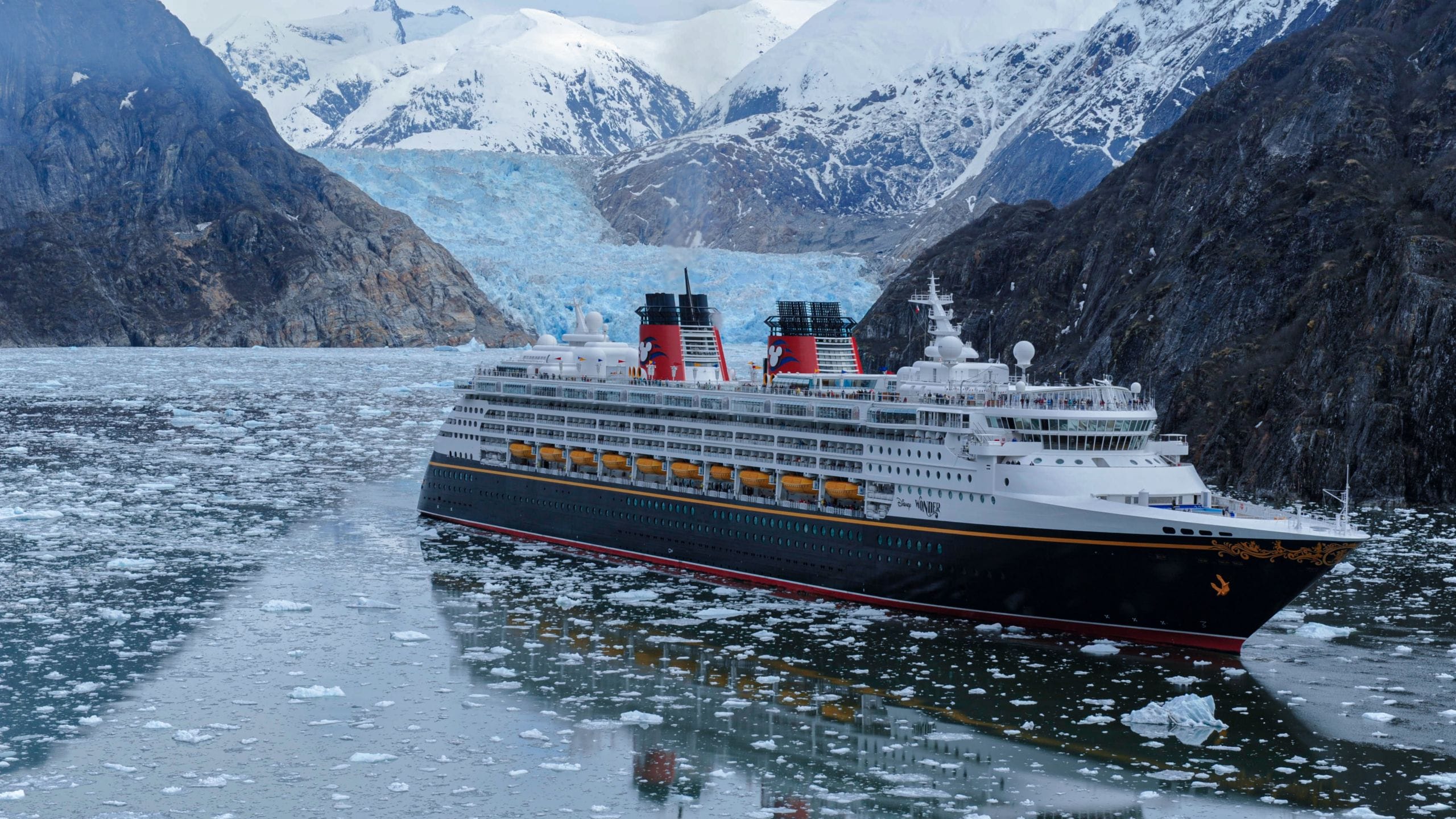 O navio de cruzeiro Disney Wonder navegando junto a montanhas cobertas de neve